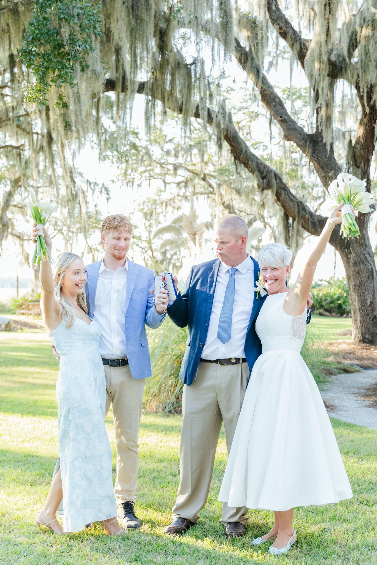 Wedding party celebrates joyfully under Spanish moss-draped trees in a garden setting.