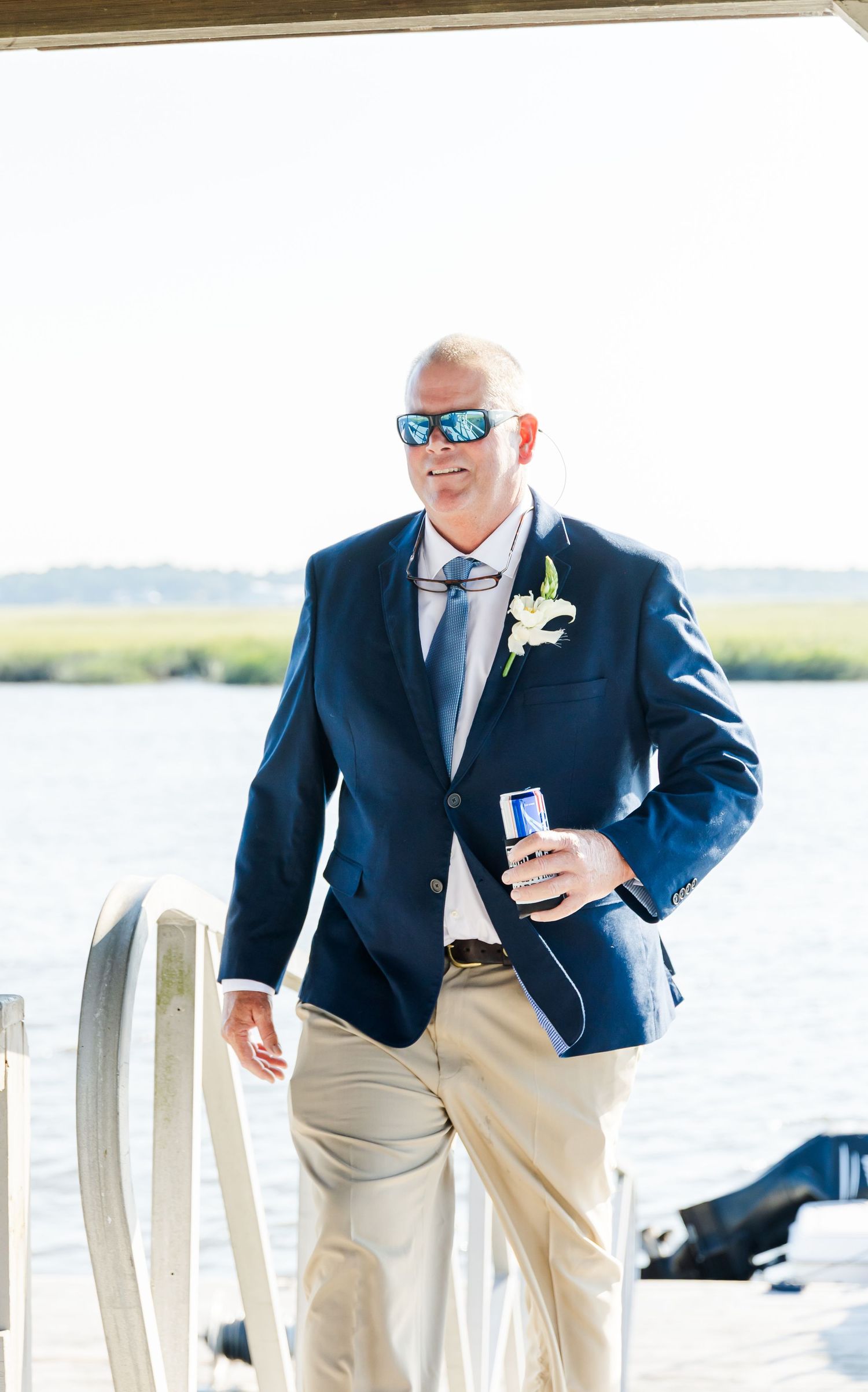People in navy blazers and khaki pants standing on a dock by the water.