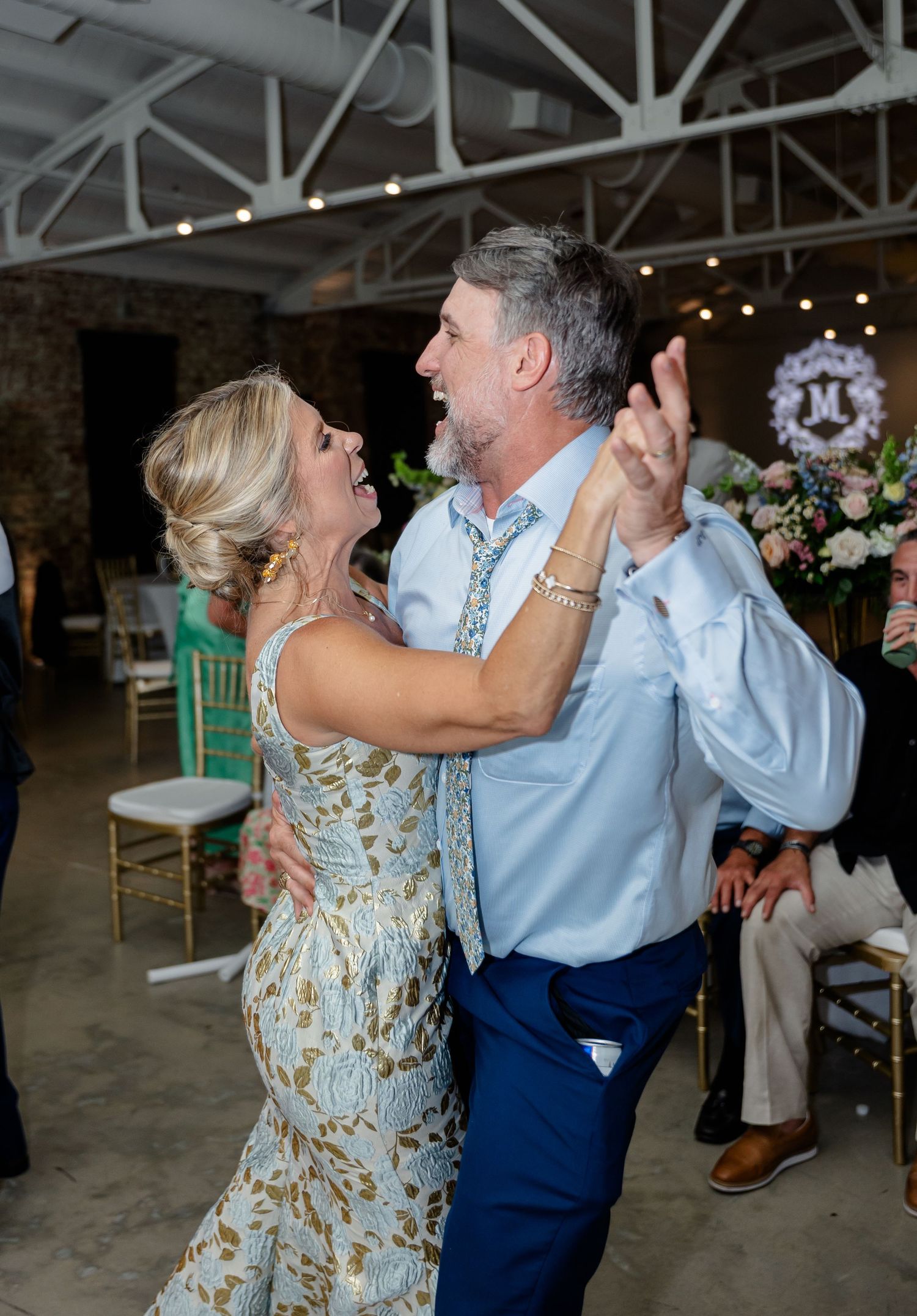 A couple dances joyfully together at a wedding reception in a rustic brick venue with exposed beams and string lights.