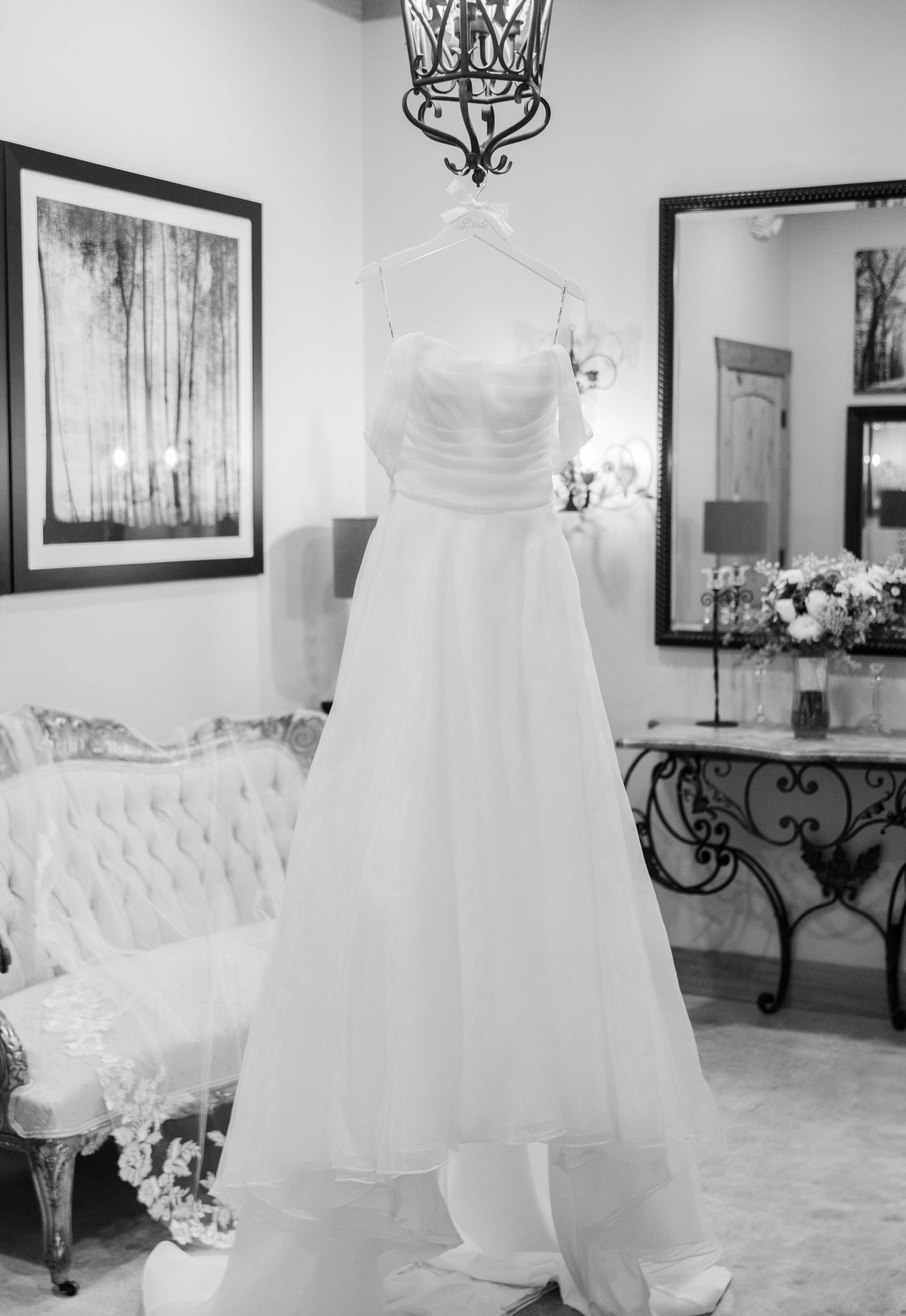 A collection of elegant white wedding dresses displayed in a room with framed artwork and ornate furniture.