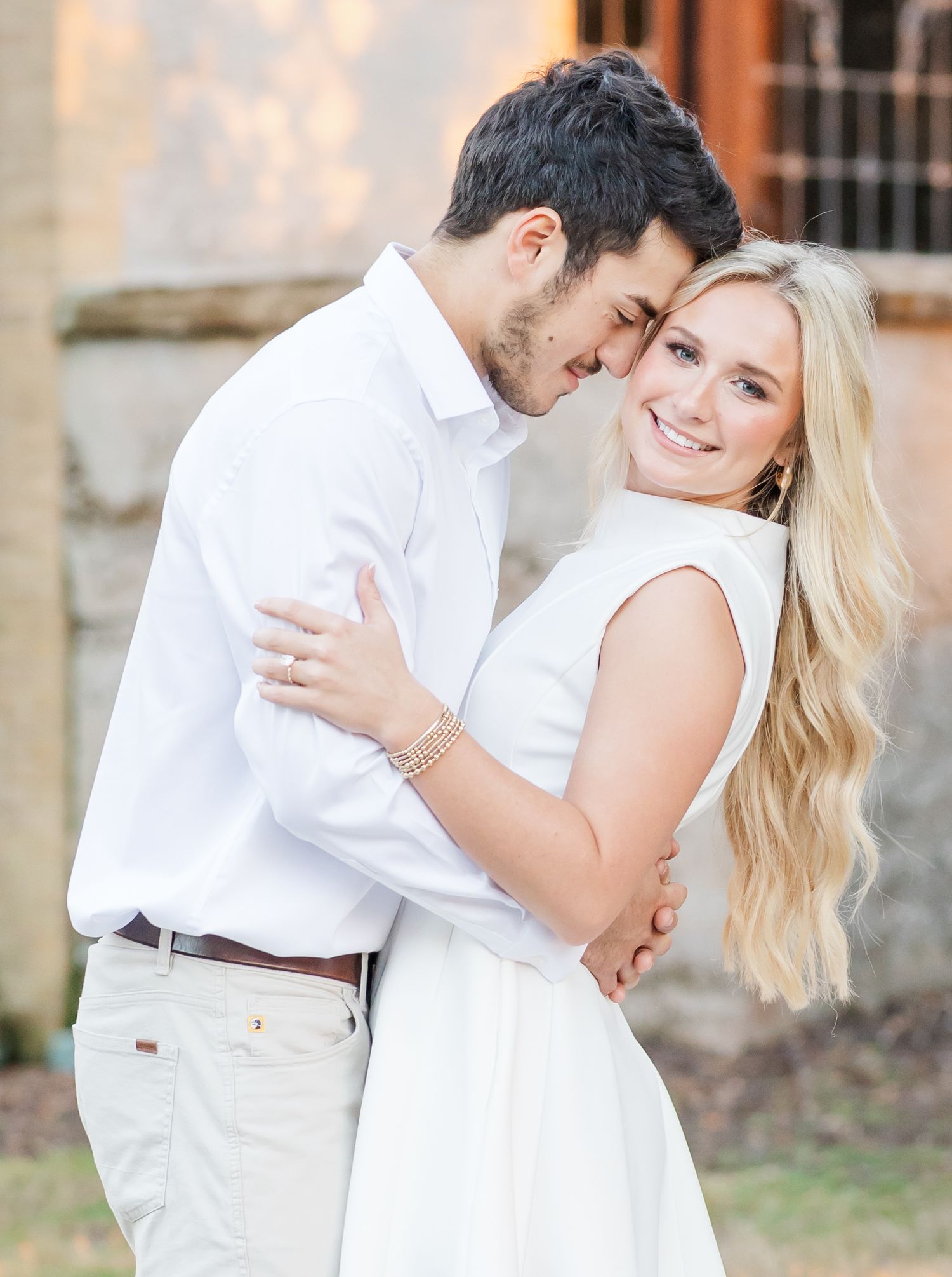 A romantic couple in white outfits embrace and dance together during an outdoor engagement photo session.