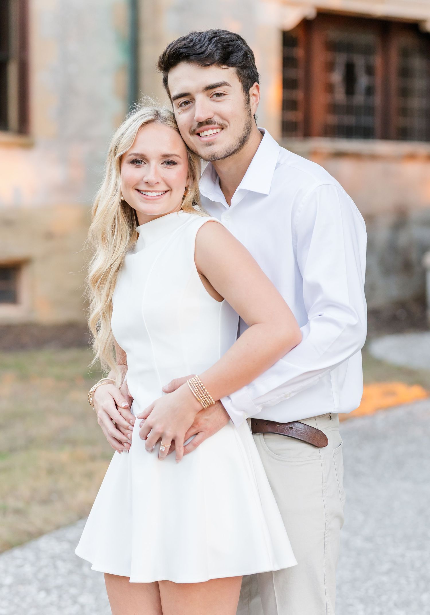 A couple in coordinating white and cream outfits embrace while posing outdoors for a romantic portrait.