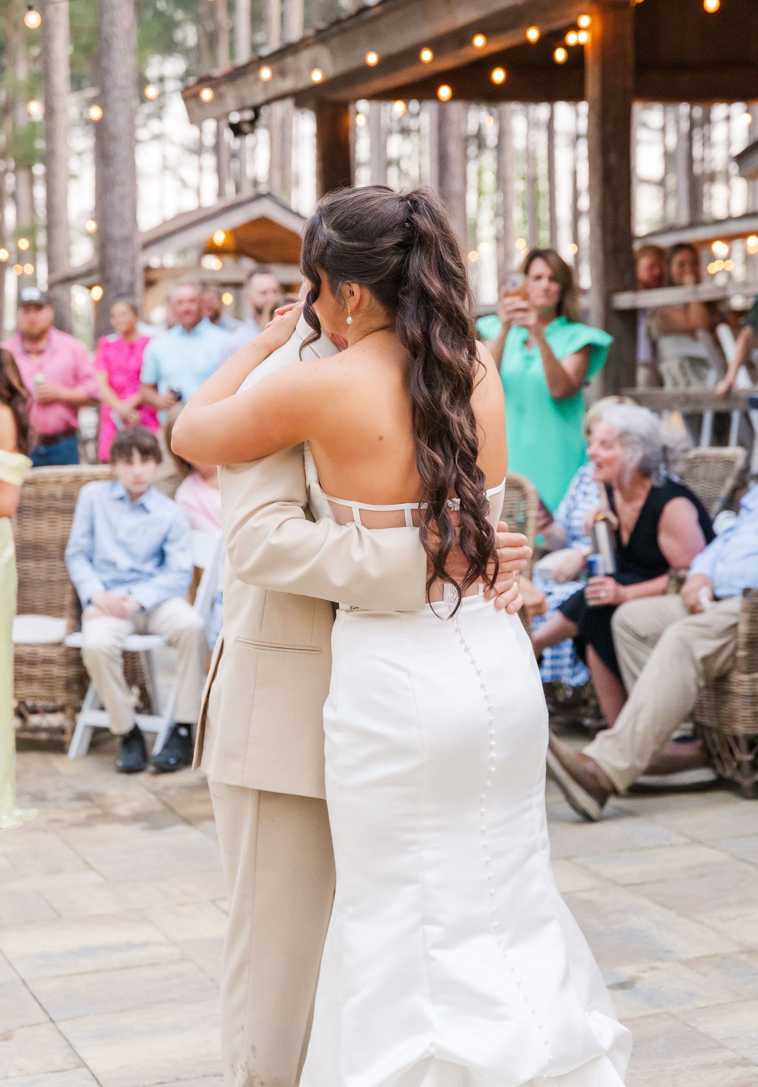Bride and groom share their first dance on outdoor patio surrounded by guests and string lights.