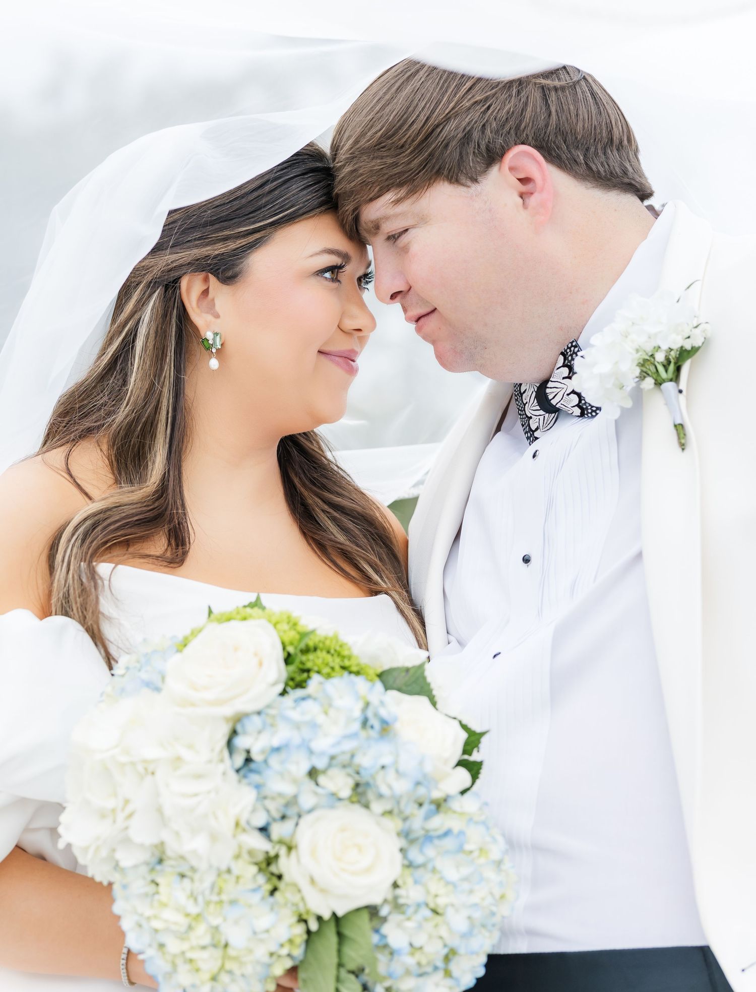 Bride and groom touch foreheads romantically, bride holding blue hydrangea and white rose bouquet.