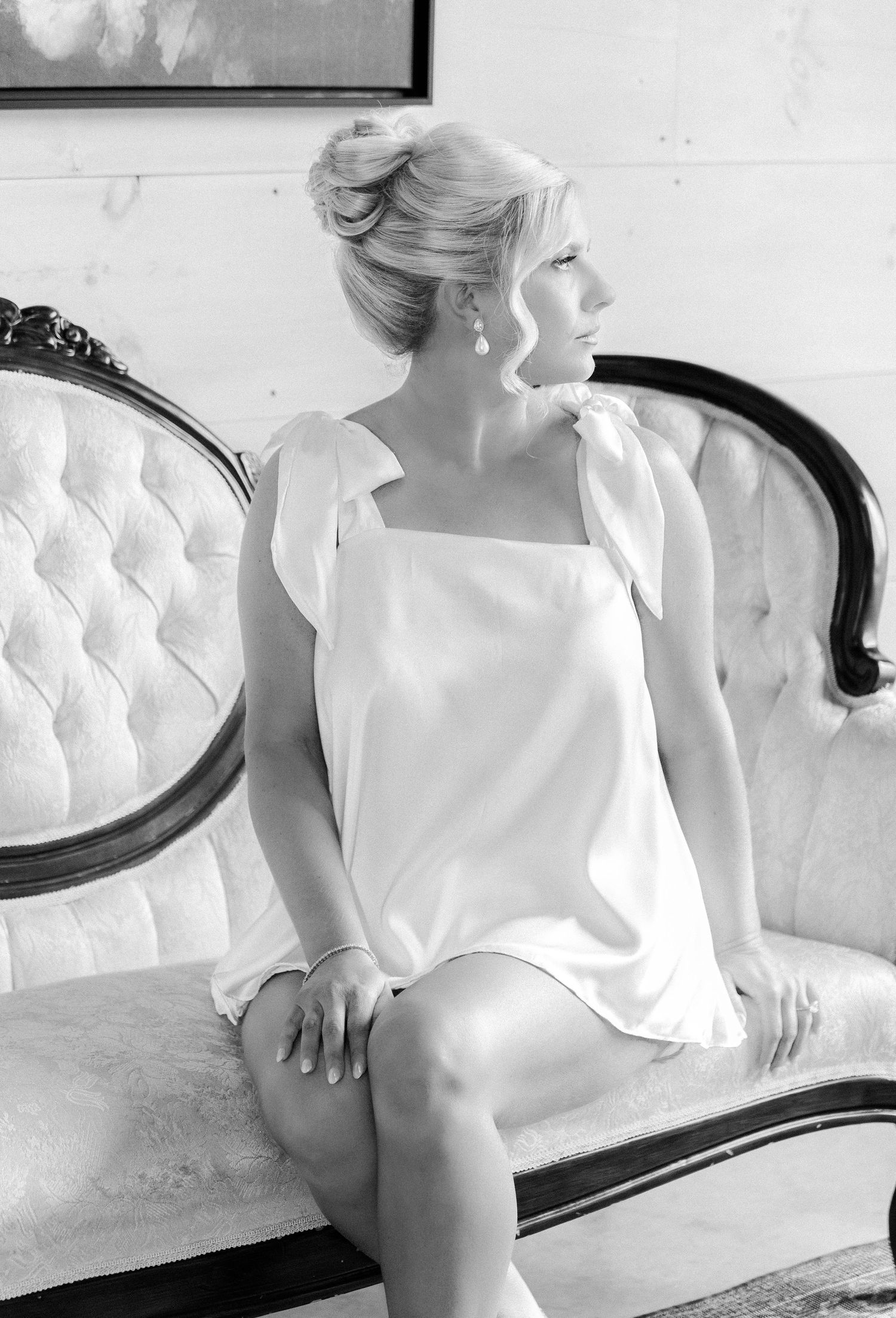 Black and white portrait of someone in a white dress sitting elegantly on a tufted vintage sofa.