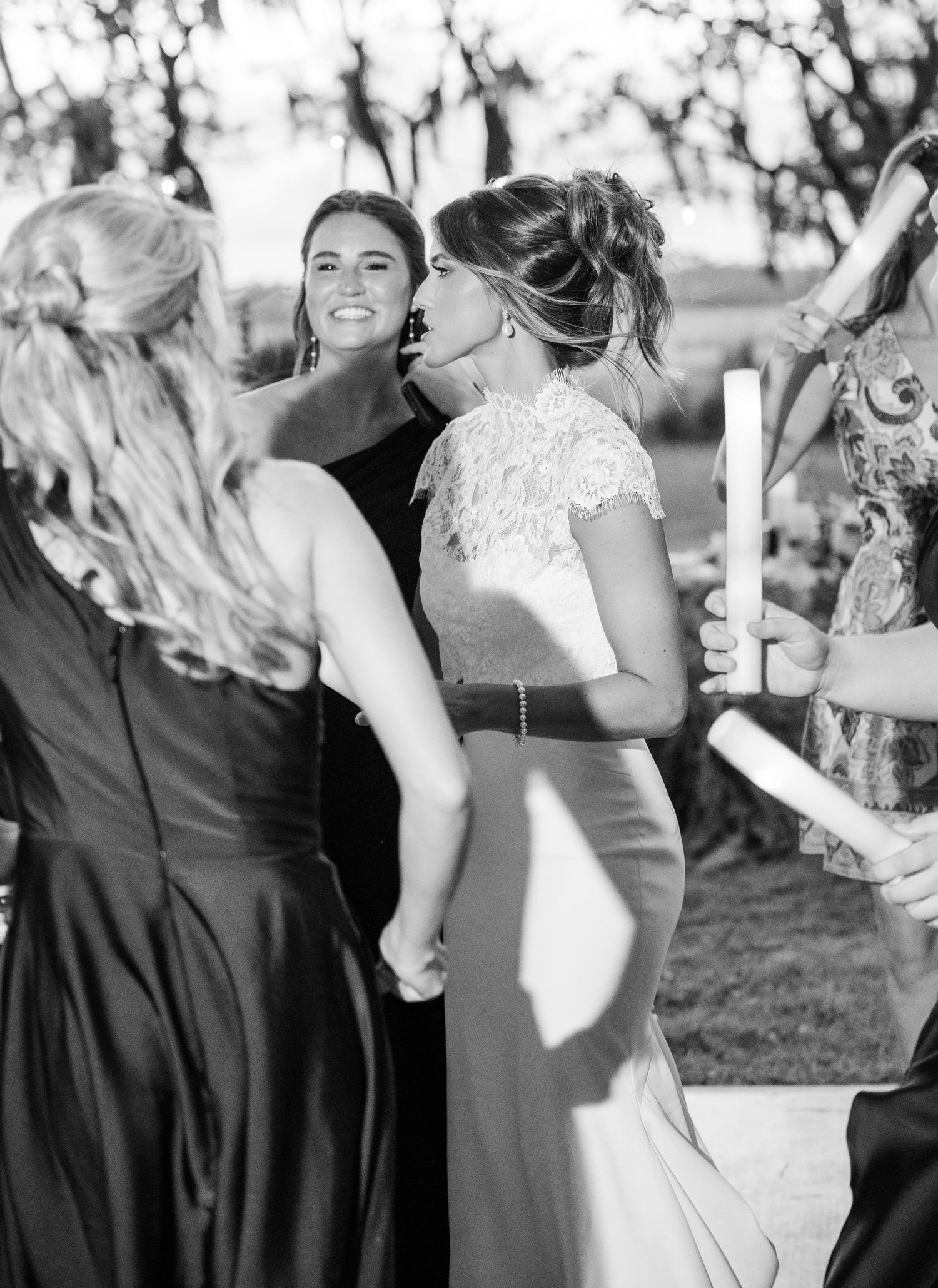 Black and white photo of bridesmaids holding candles and hands at an outdoor wedding ceremony.
