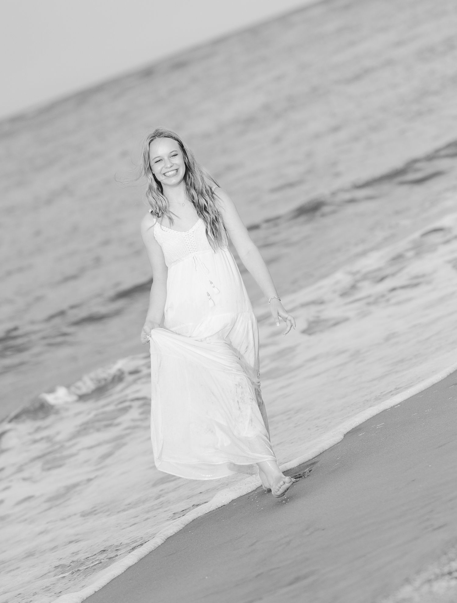 A black and white beach portrait with waves and flowing dress creating romantic coastal atmosphere.