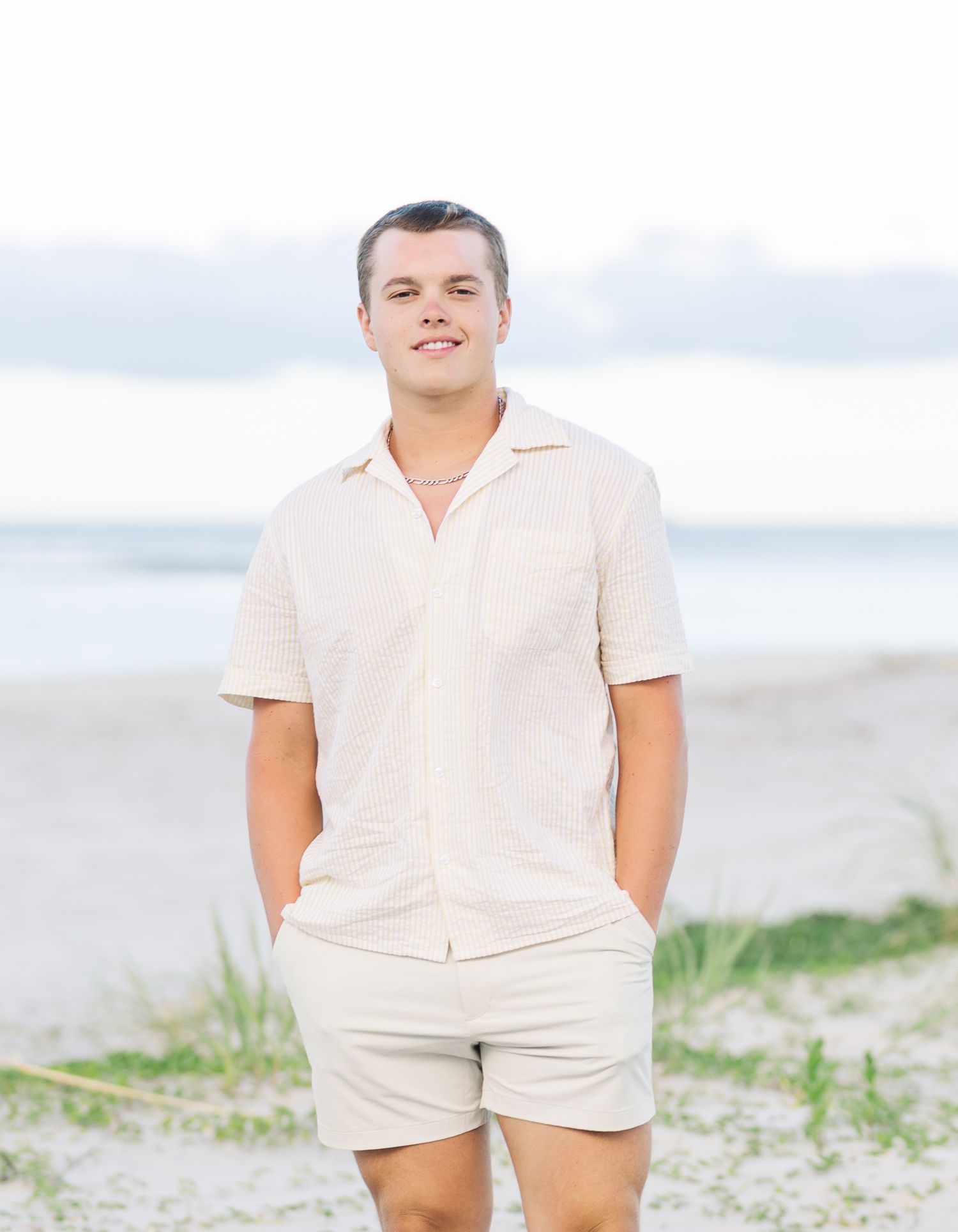 People in light colored summer clothing pose casually on a beach with dunes in the background.