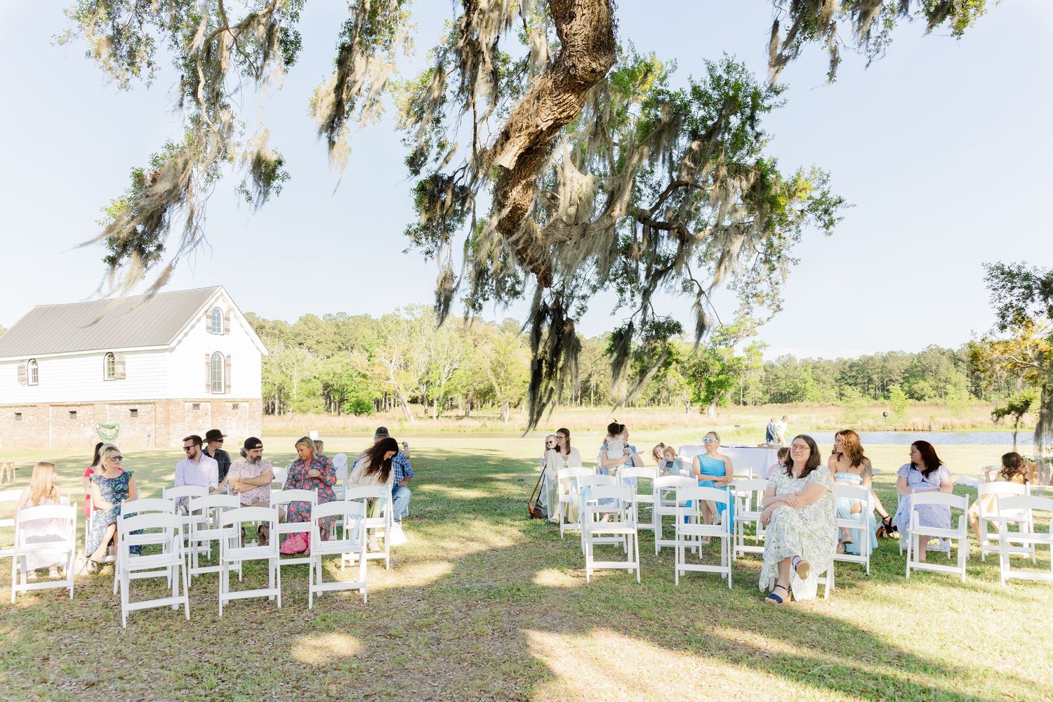 Small outdoor wedding ceremony with white chairs under Spanish moss-draped oak tree.