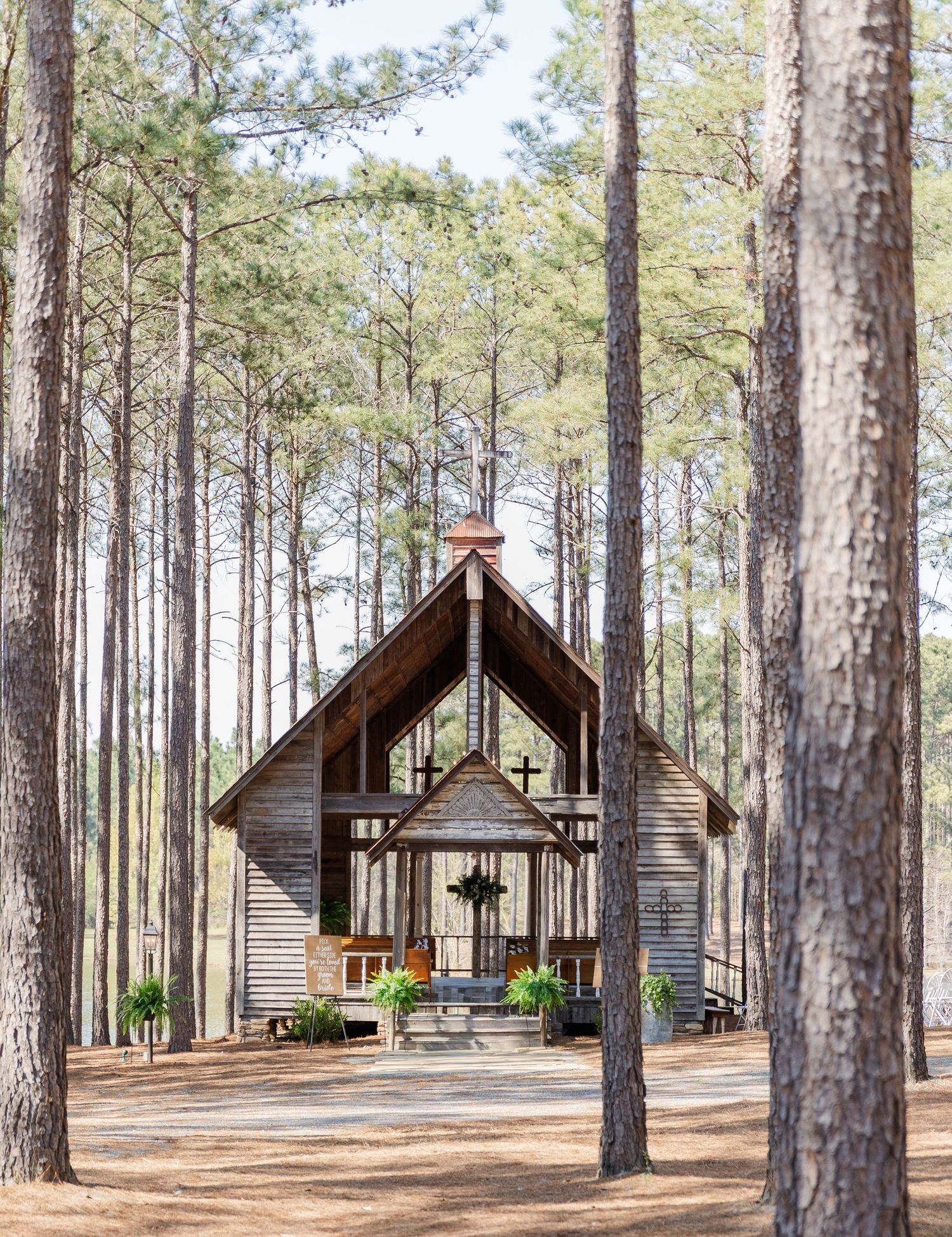 Rustic wooden chapel with a cross nestled among tall pine trees in a serene forest setting.