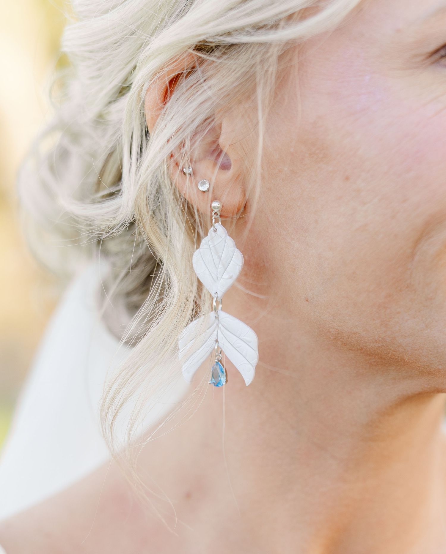Close-up of a bride wearing elegant white leaf-shaped drop earrings with blue crystal accents.