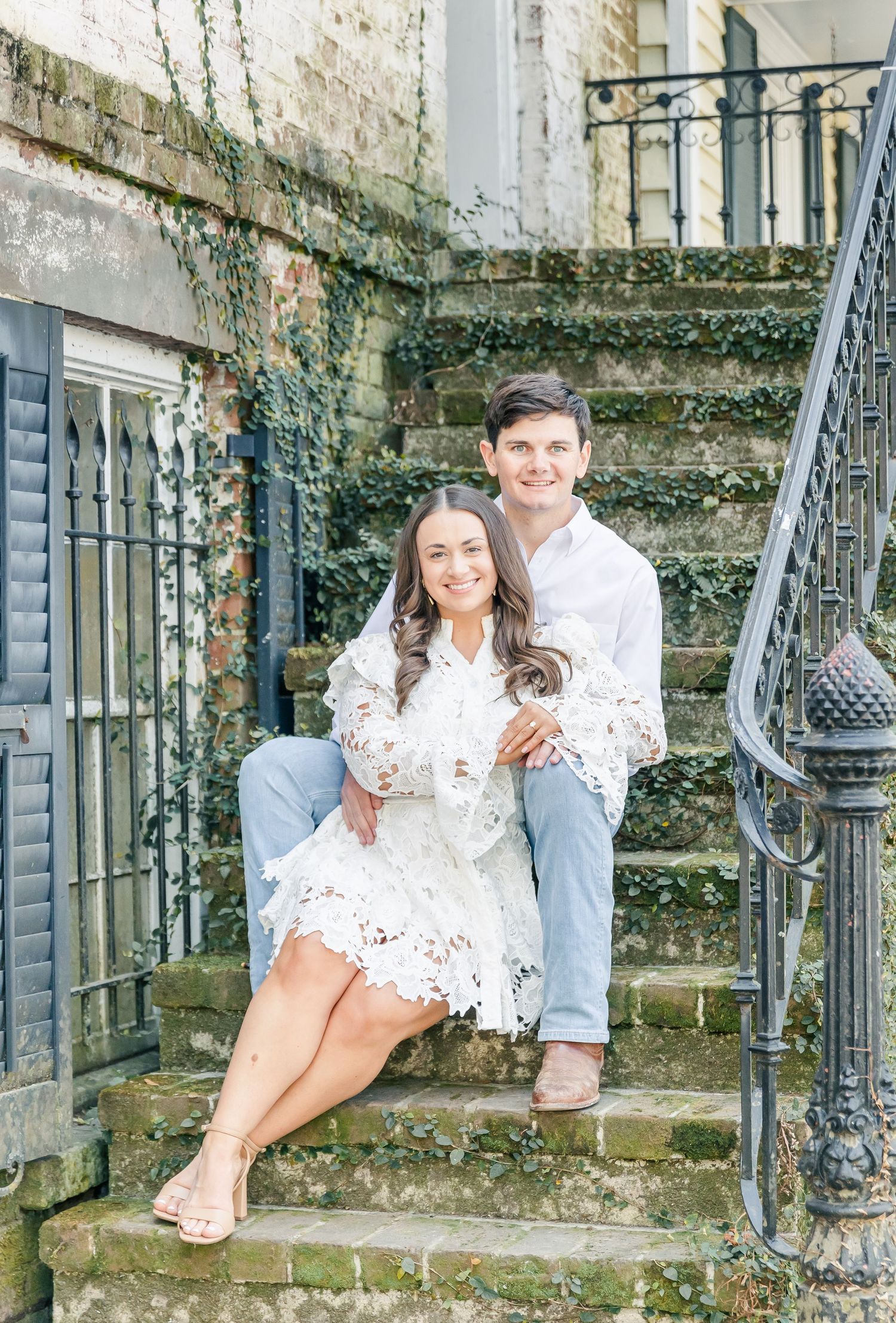 Couple sitting together on rustic stone steps with vintage wrought iron railings and ivy covered walls.