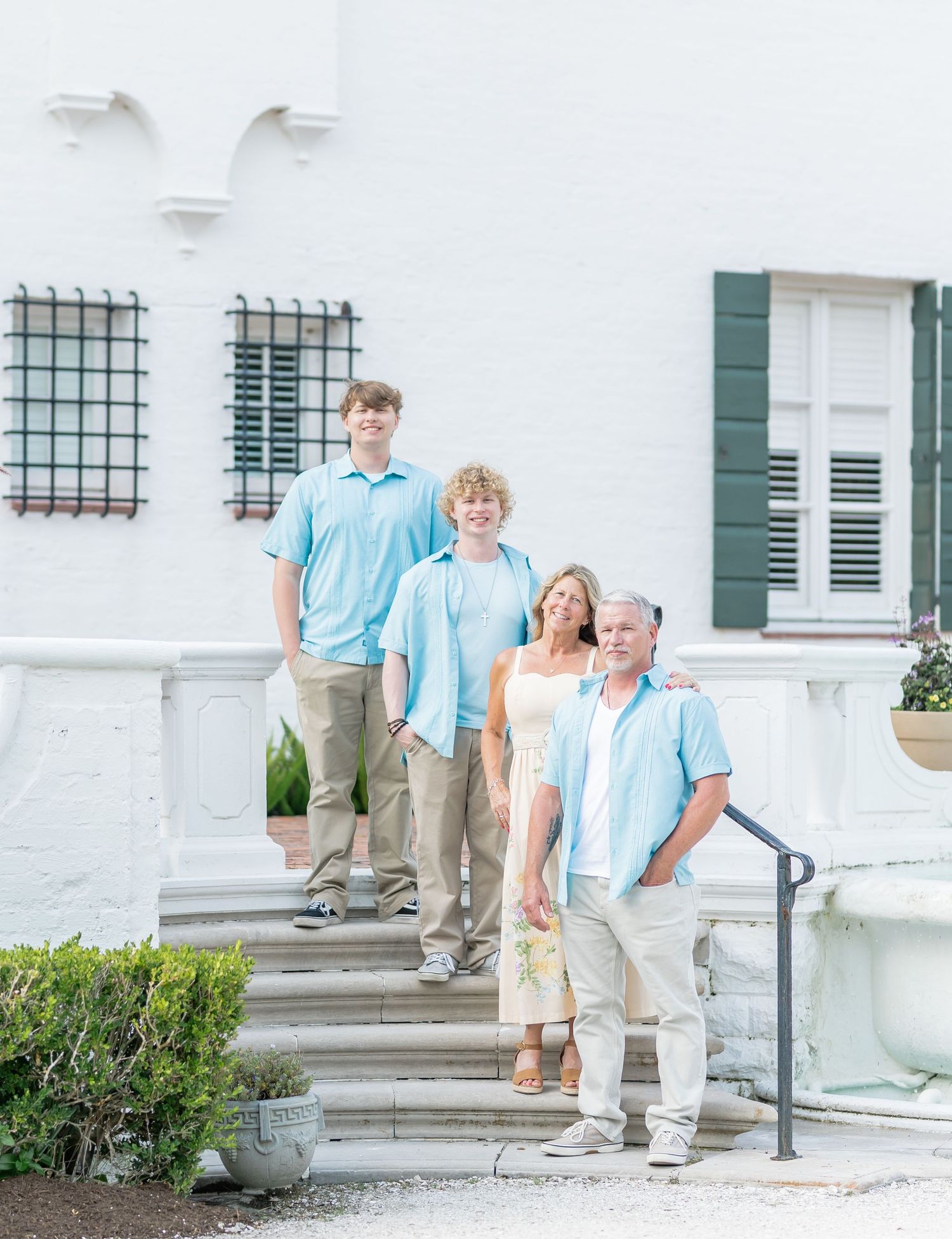 A group in matching light blue shirts and khaki pants pose on white stone steps outside a historic building.