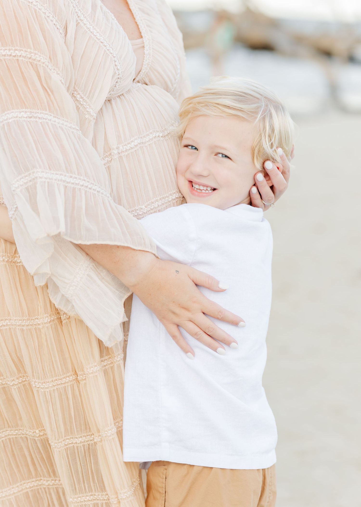 Sweet beach portrait of a child in white shirt hugging an adult in a flowing dress.