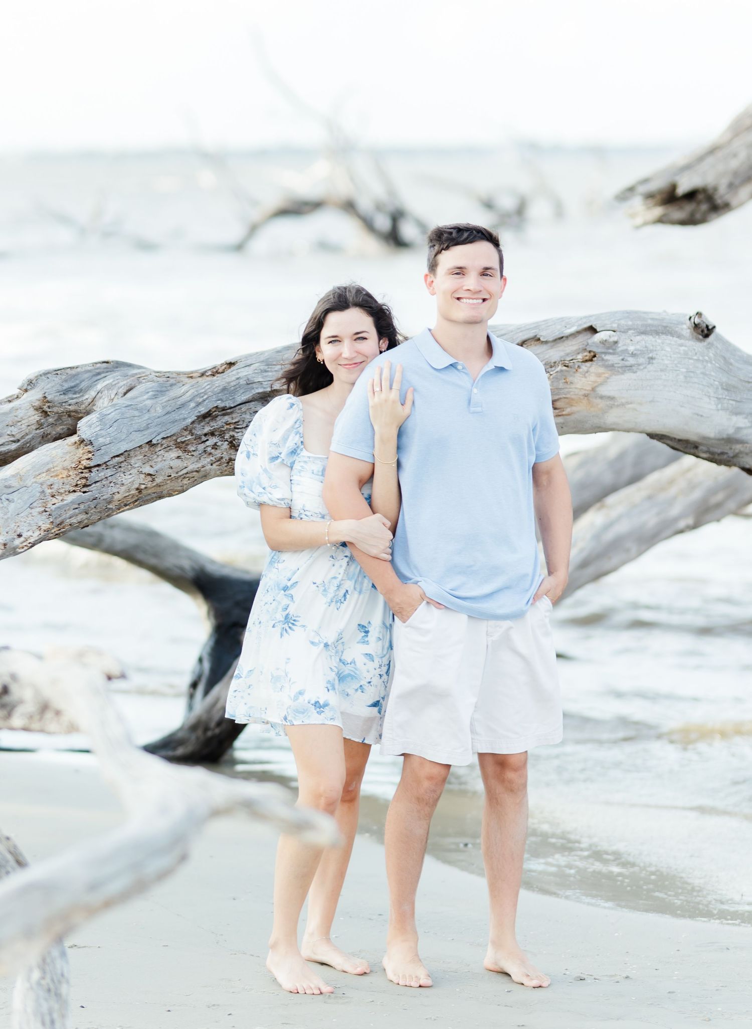 A couple poses together on rocky coastal formations with the ocean in the background.