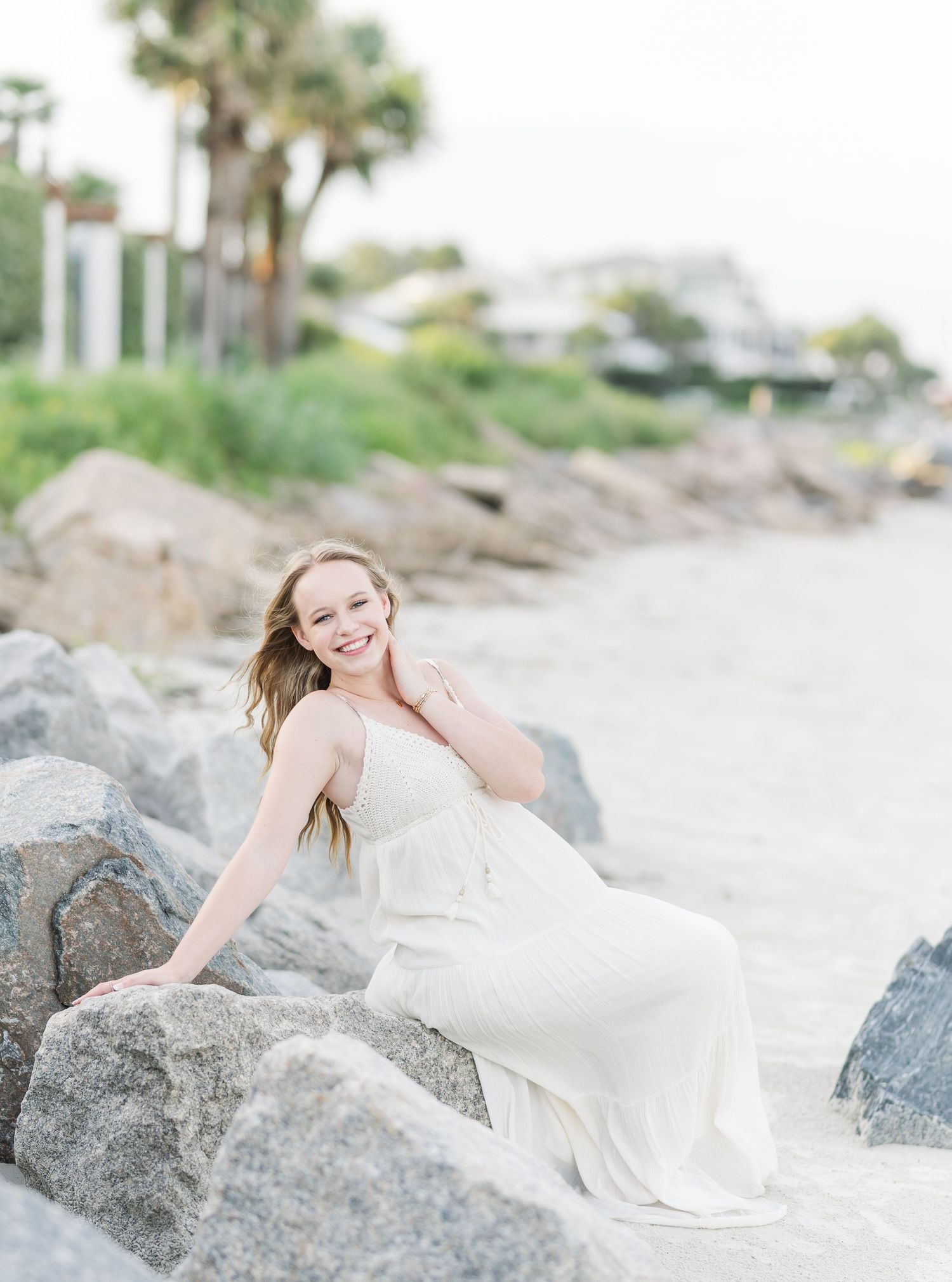 Ethereal white gown photographed on rocky beach setting with dreamy coastal lighting.