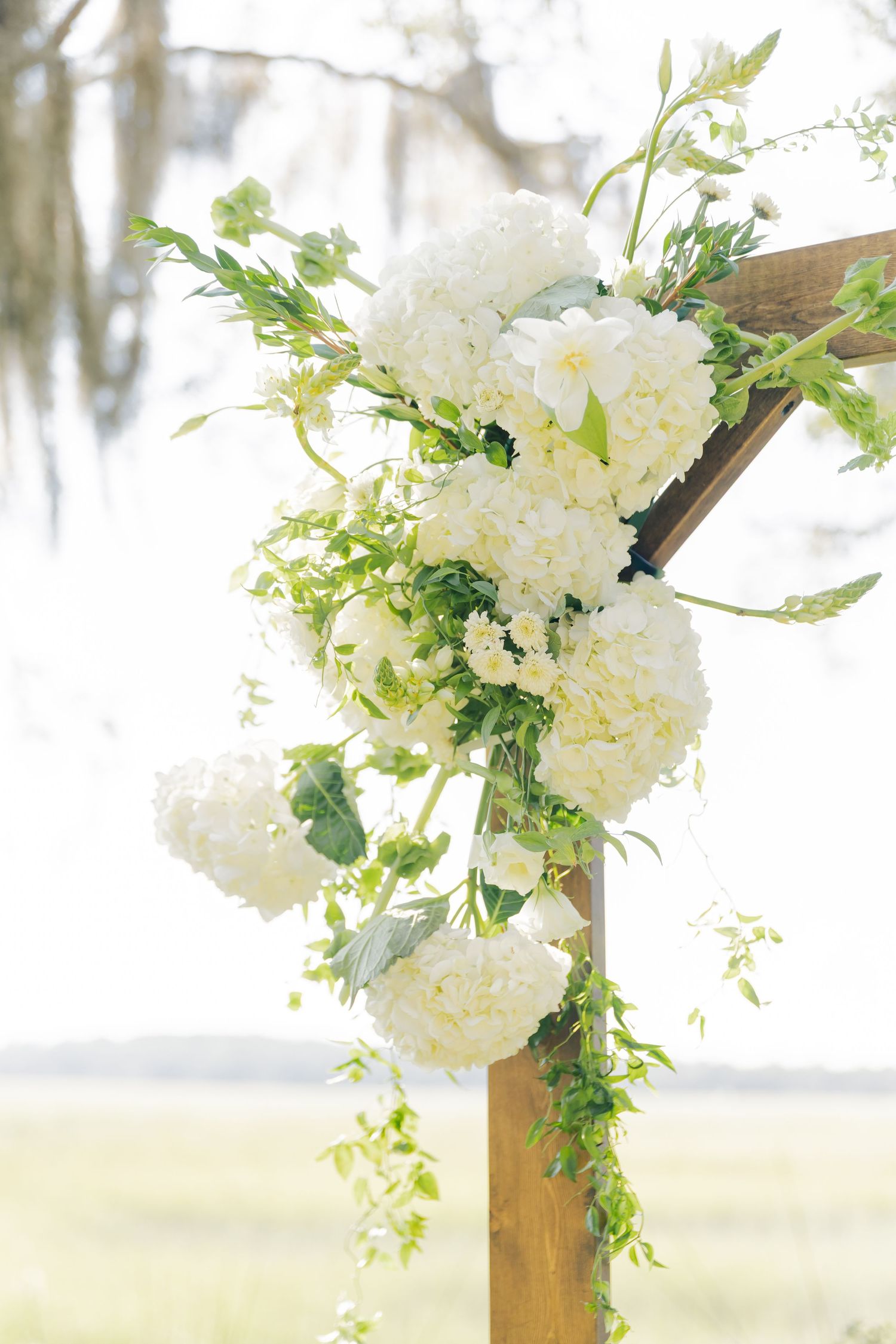 White hydrangeas and greenery decorate a wooden arch frame in an elegant outdoor wedding ceremony setup.