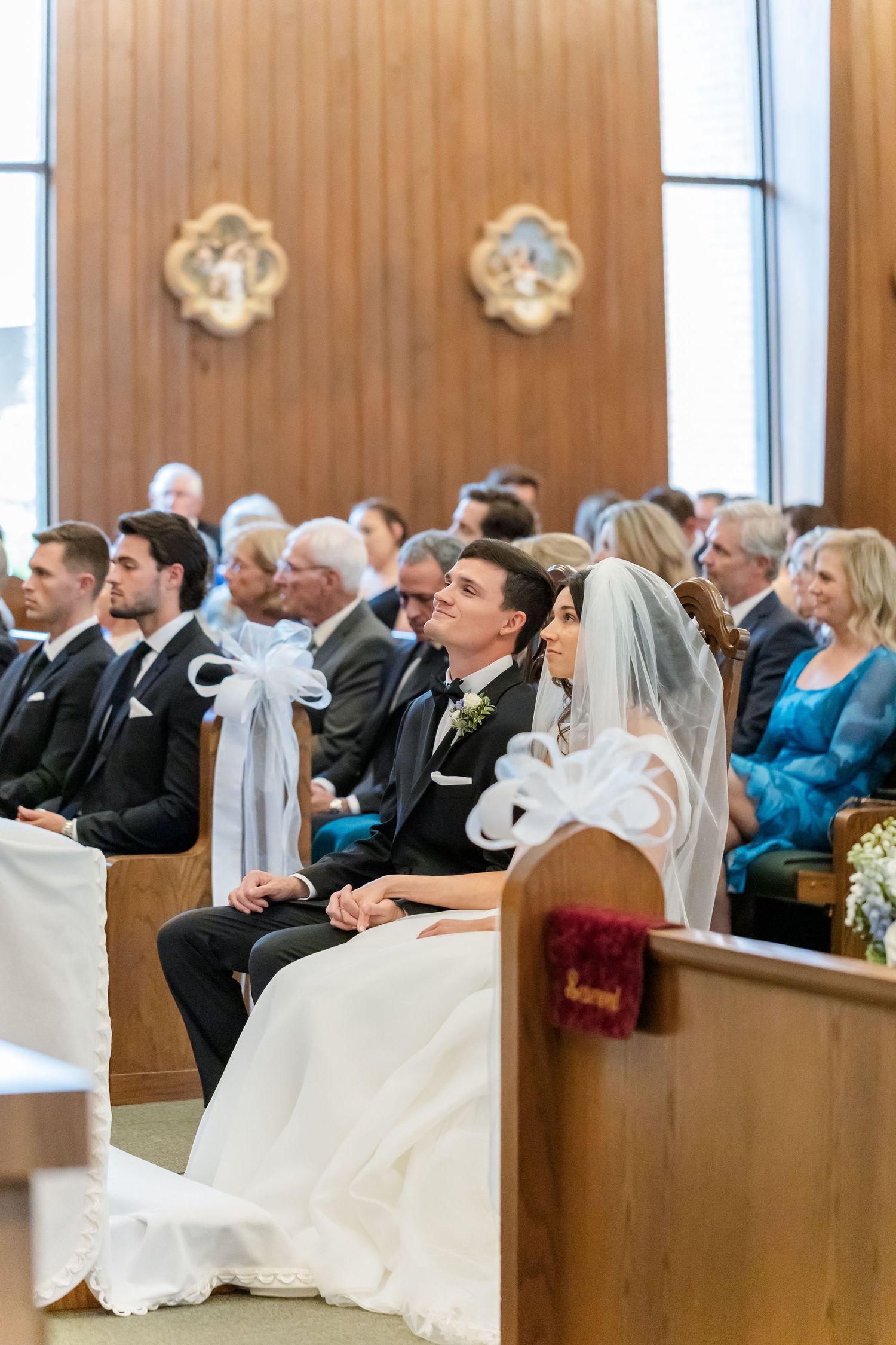 Wedding ceremony in progress inside a church with wood paneled walls and filled pews.