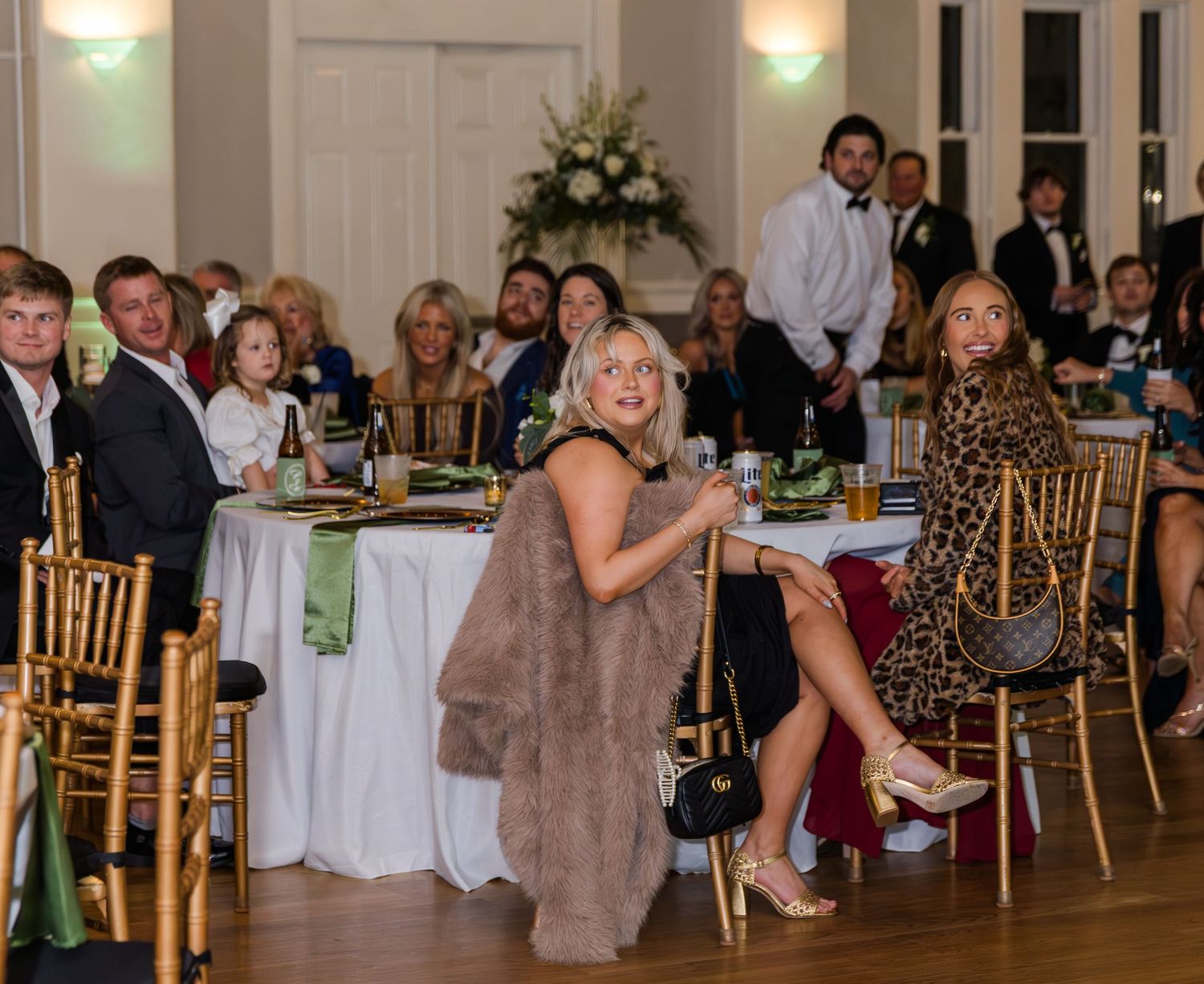 Elegant wedding reception guests seated at decorated tables in a grand ballroom with floral arrangements.