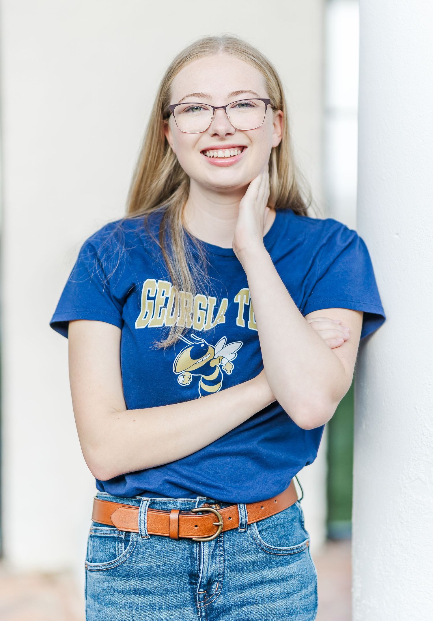 Person in collegiate t-shirt smiles brightly while posing against white architectural background.
