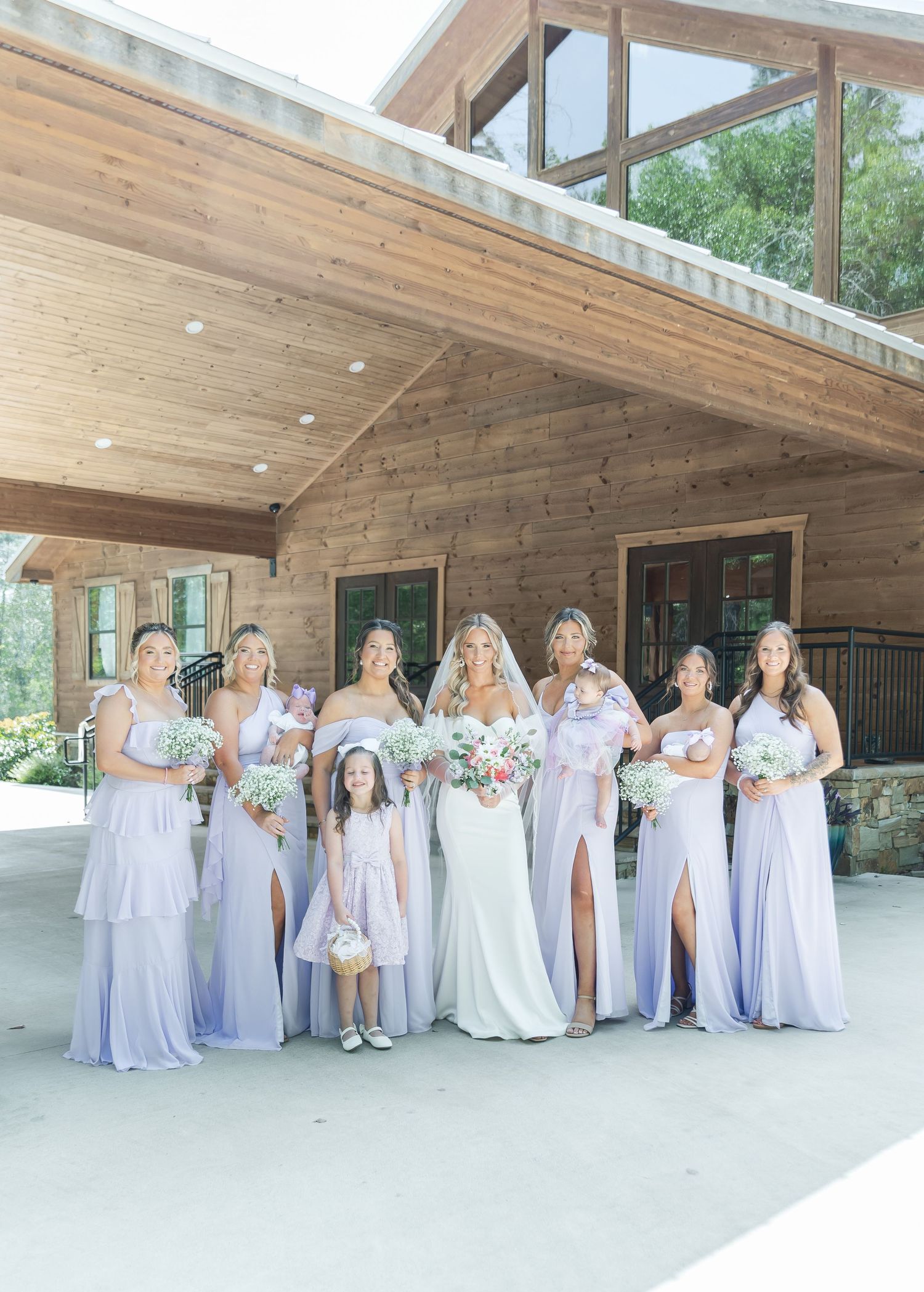 Full bridal party in lavender dresses stands together on rustic wooden porch during wedding.