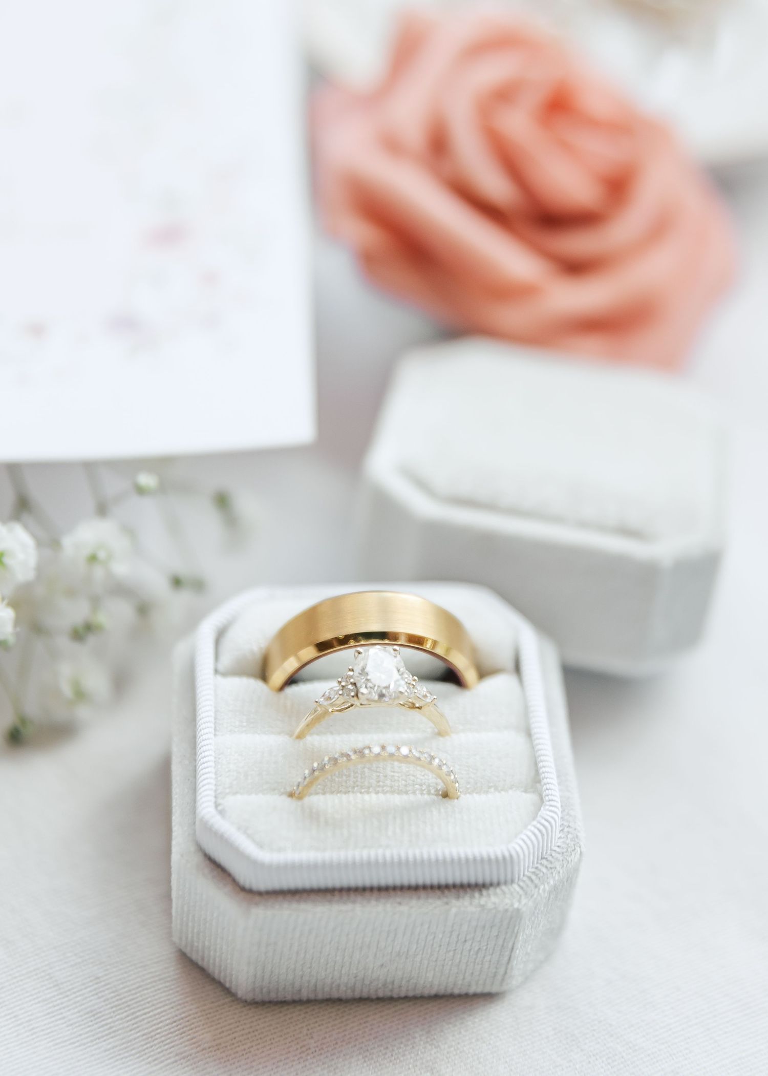 Gold and diamond wedding rings nestled in a white velvet ring box with pink roses.