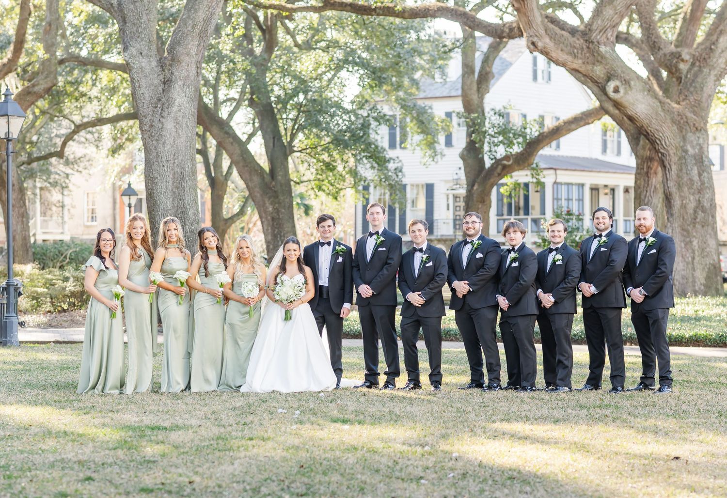 Wedding party posing under large oak trees in a garden setting.