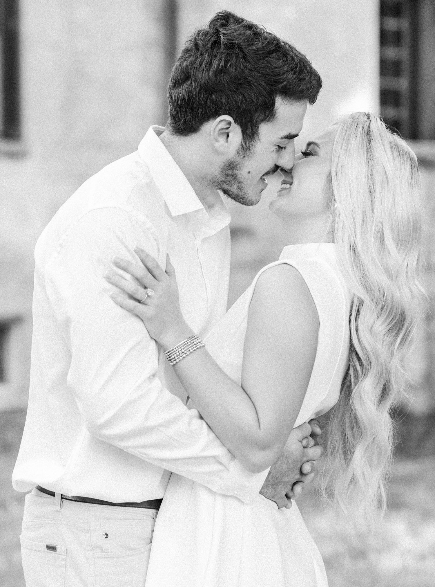 Black and white intimate portrait of couple sharing tender moment against architectural backdrop.