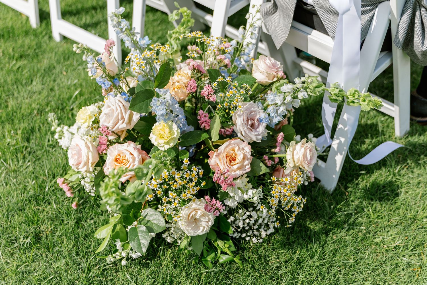 Elegant floral arrangements with pink and peach blooms line a white garden fence at an outdoor wedding venue.