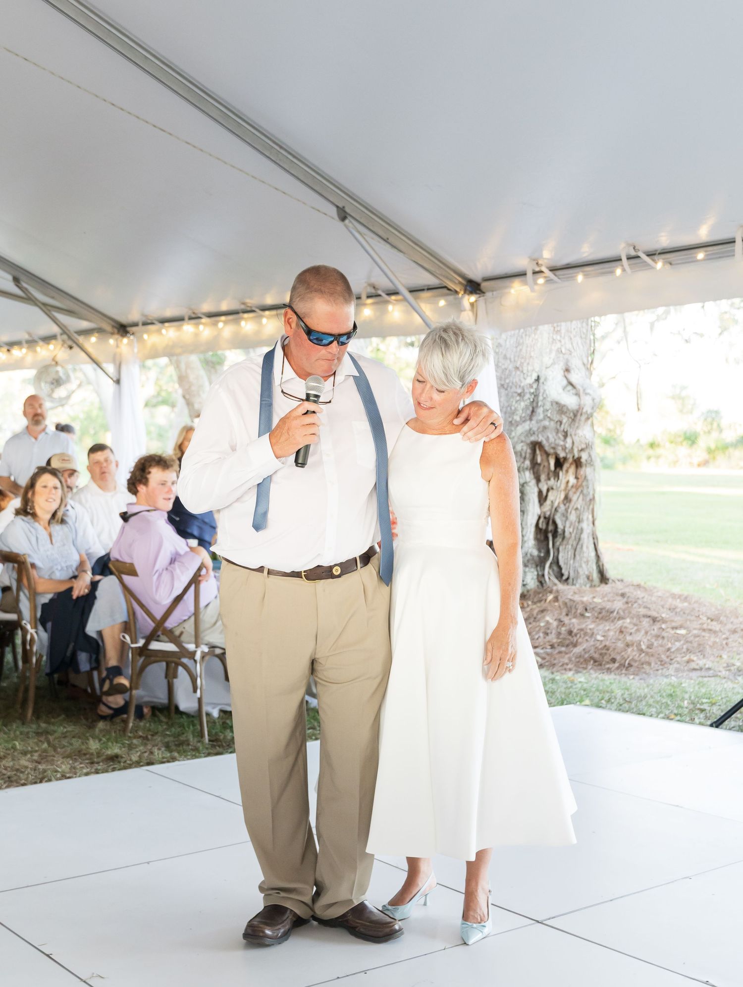 Wedding guests dance together under a white tent during a reception celebration.