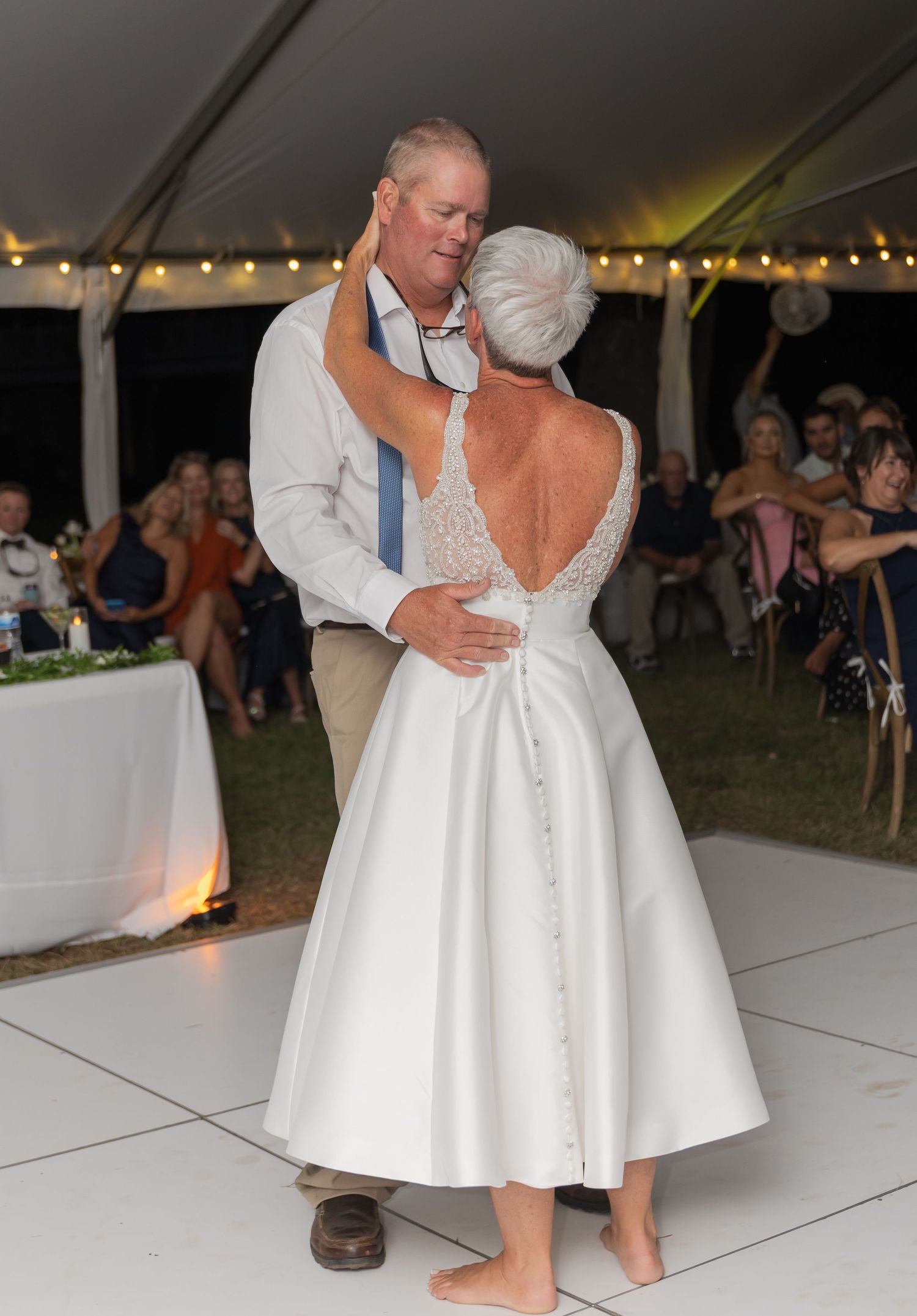 Couple dancing in formal attire on a white dance floor at an outdoor wedding reception.