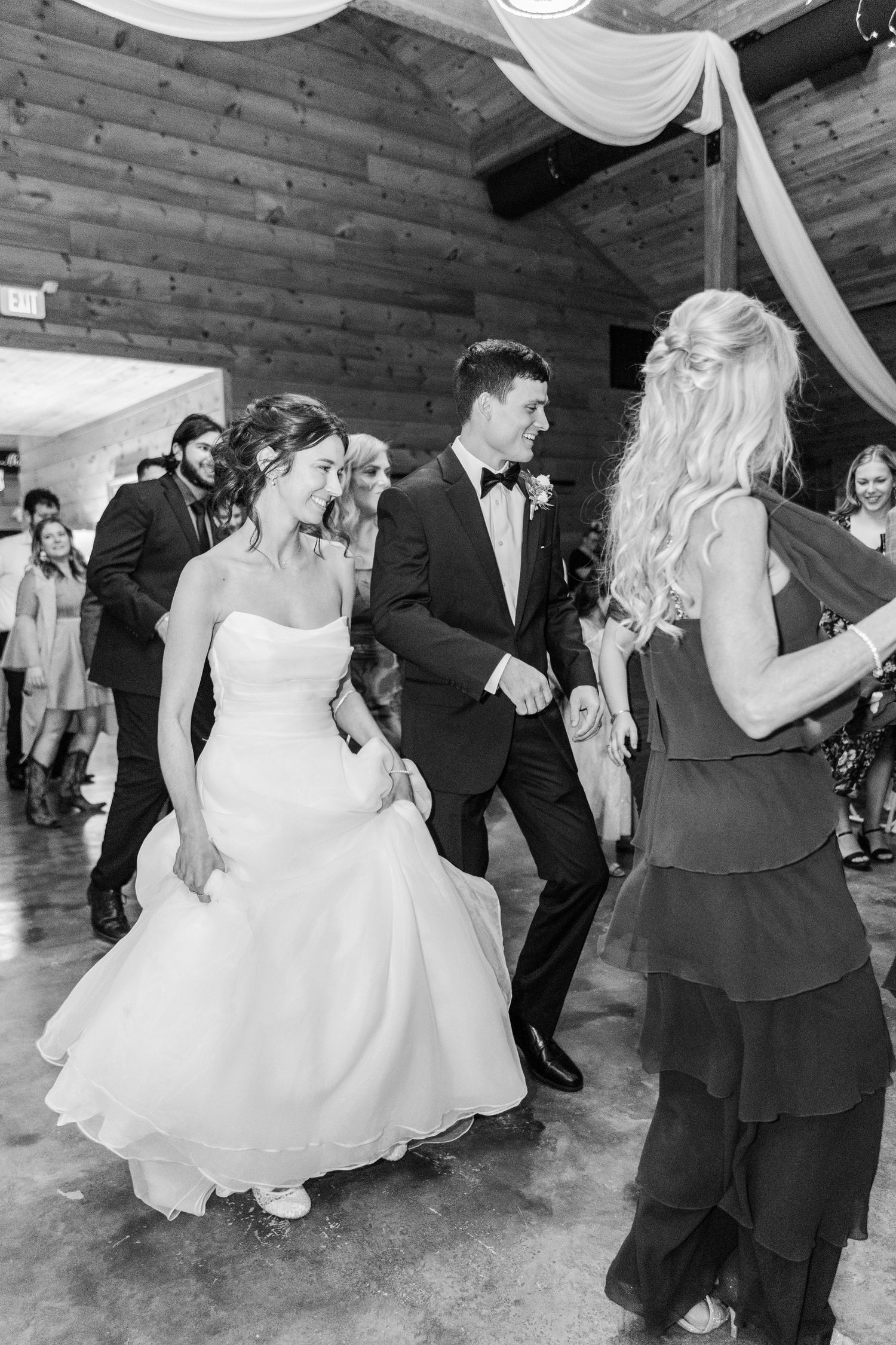 Wedding party dances energetically on wooden floor during reception celebration.