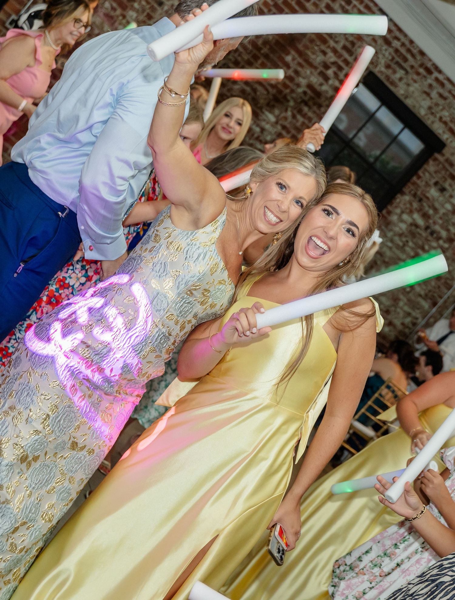 Party guests dance with illuminated LED foam sticks creating colorful light trails.