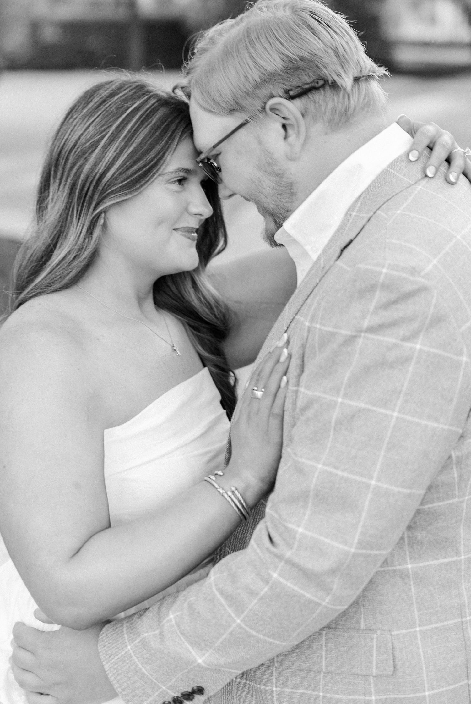 Black and white photo of a couple in wedding attire sharing an intimate moment, foreheads touching and smiling at each other.