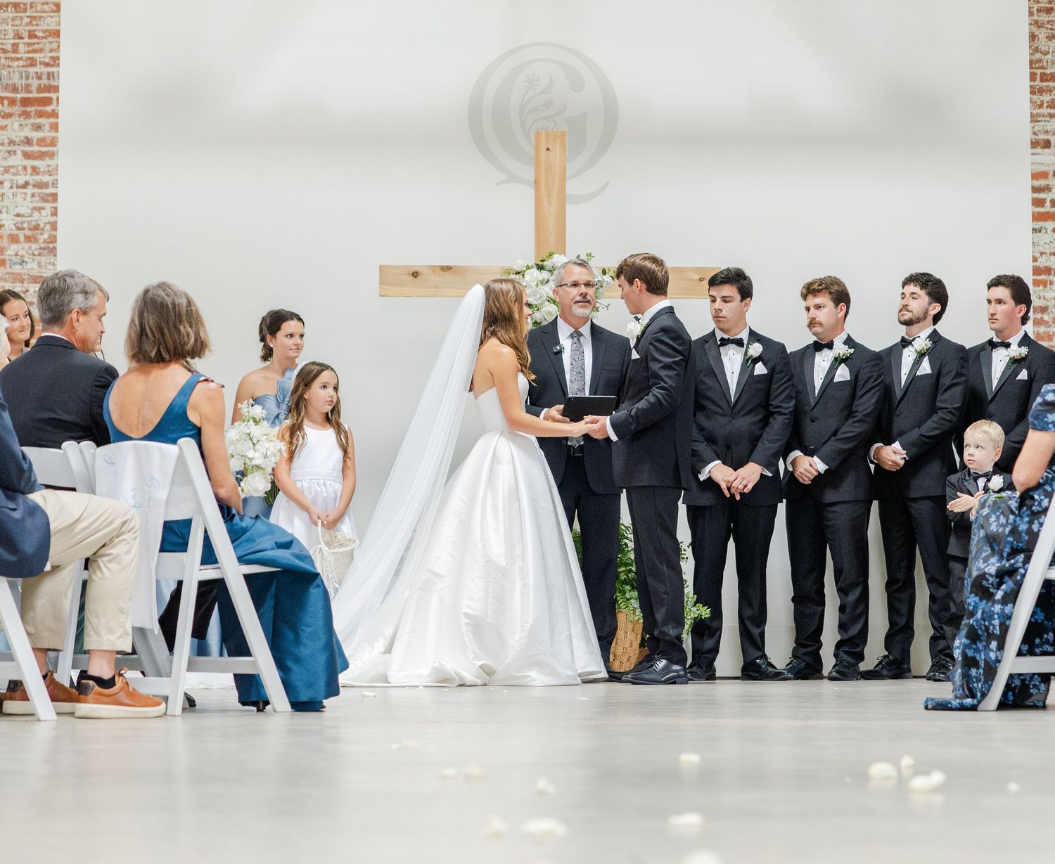 Bride and groom exchange vows at elegant indoor wedding ceremony with wooden cross backdrop.