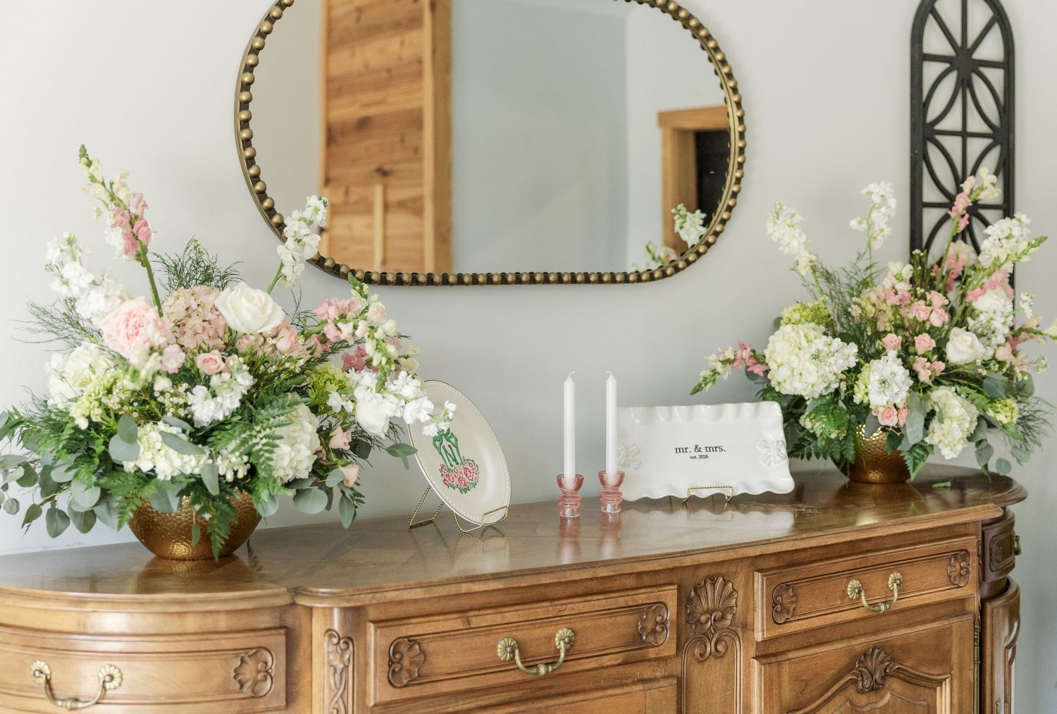 Ornate wooden dresser with gold floral arrangements, pink candles, and mirror in elegant wedding decor.