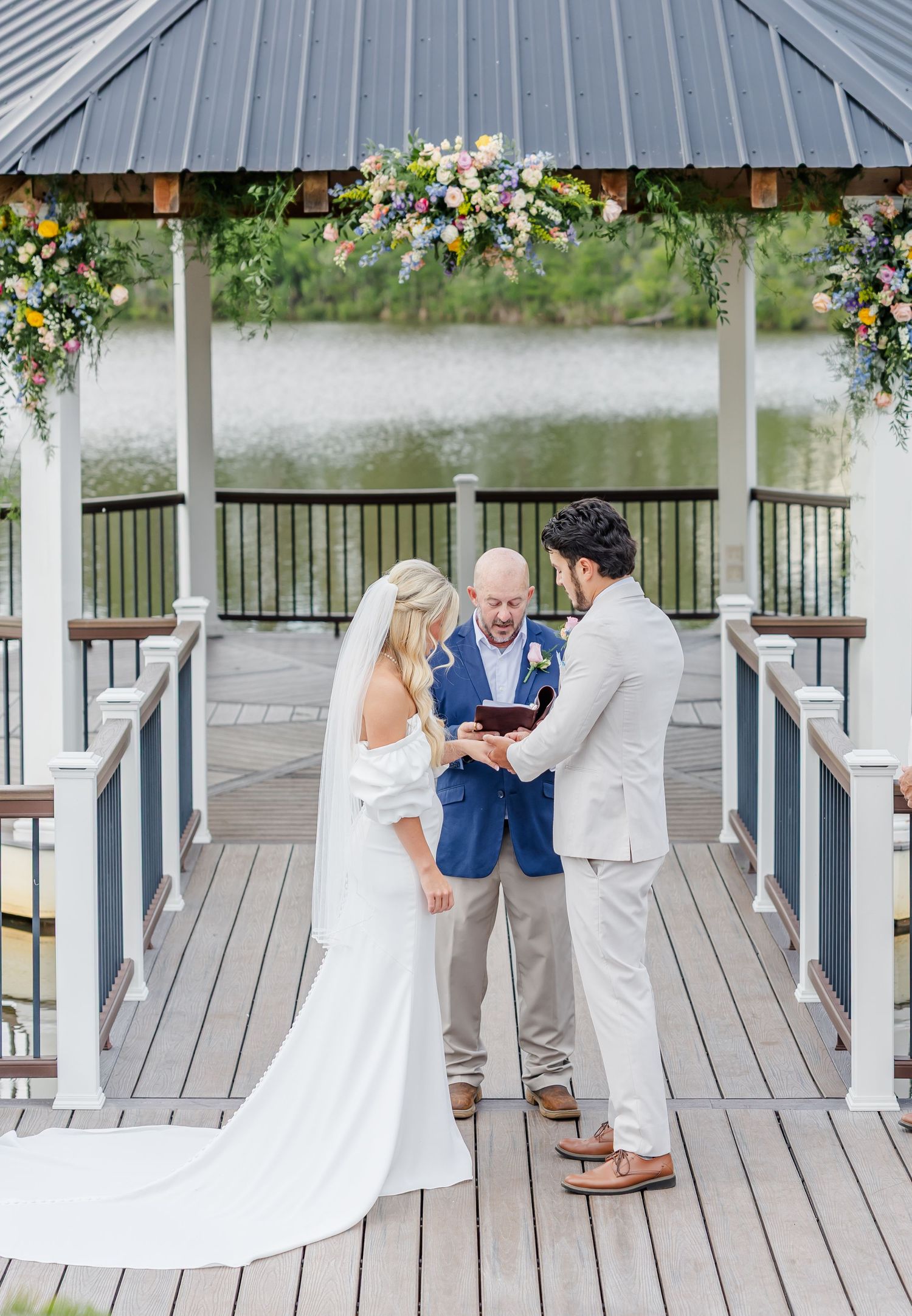 Bride and groom exchange vows in decorated gazebo overlooking water at outdoor wedding.
