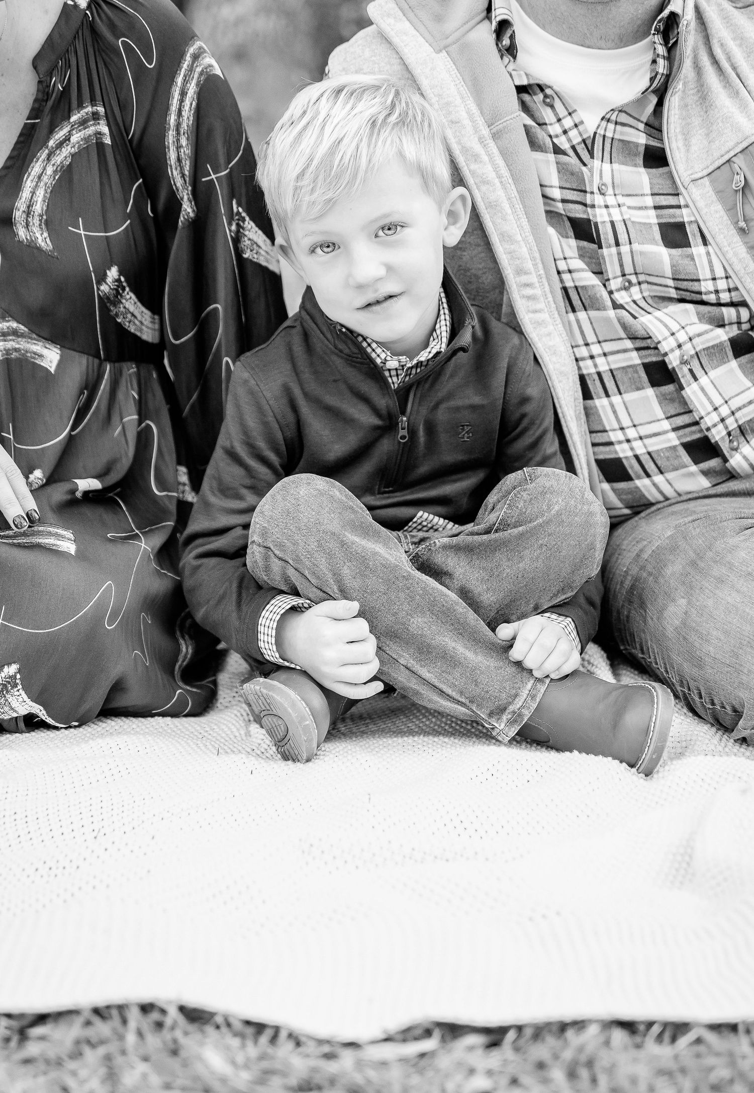 Black and white close-up of young child sitting on blanket outdoors.