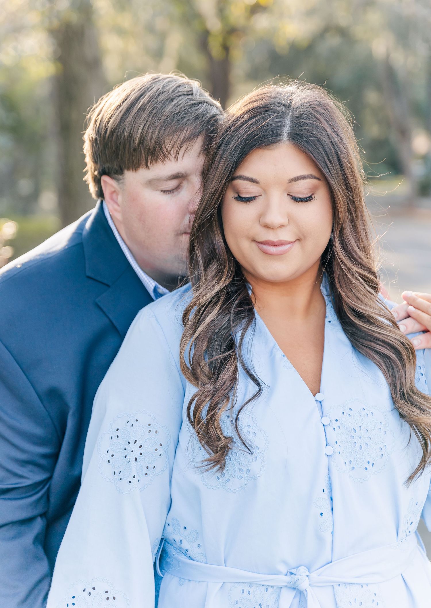 A romantic close-up portrait of a couple in light blue and navy sharing an intimate moment outdoors.