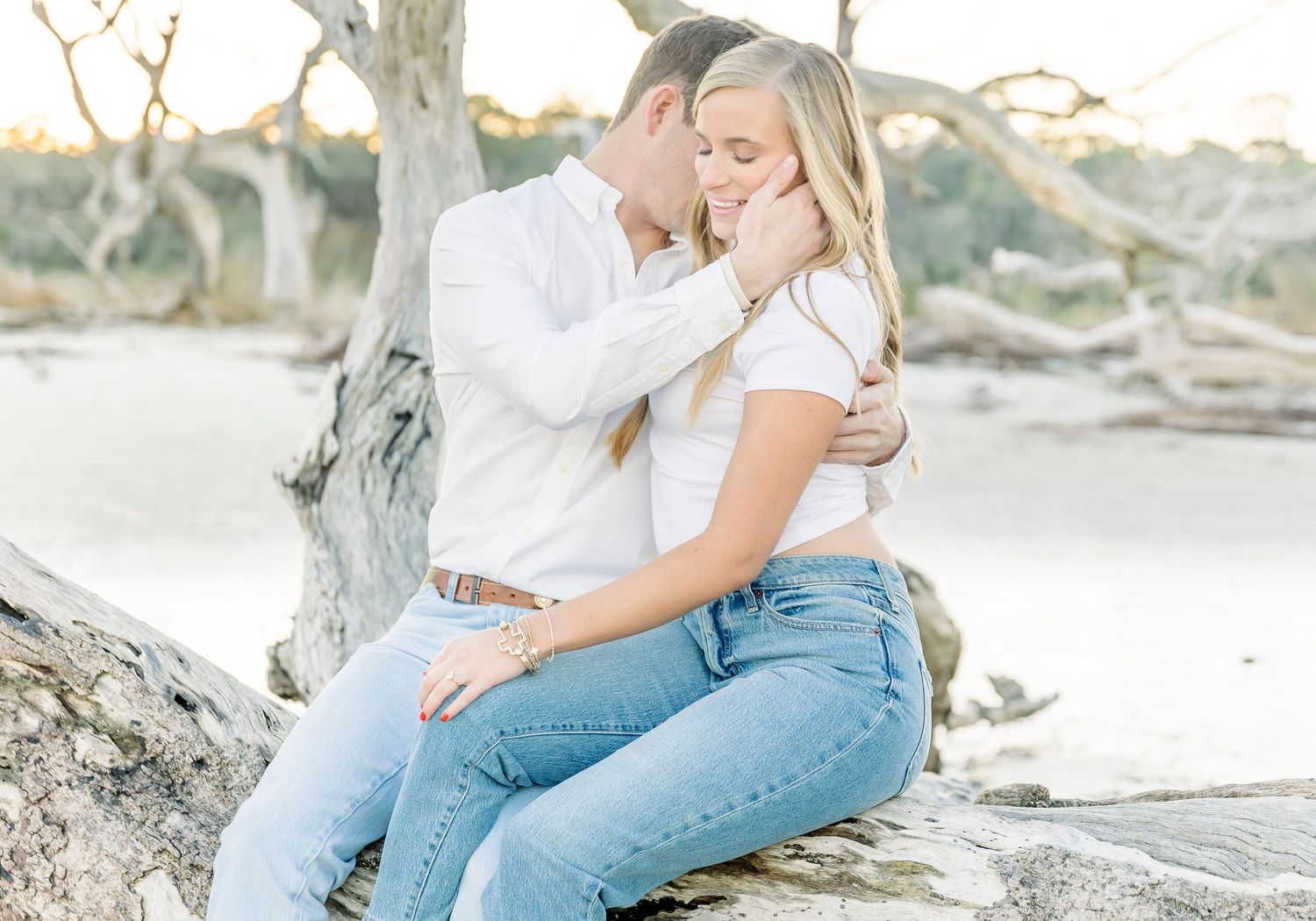 A couple shares tender moment while sitting on driftwood at the beach.