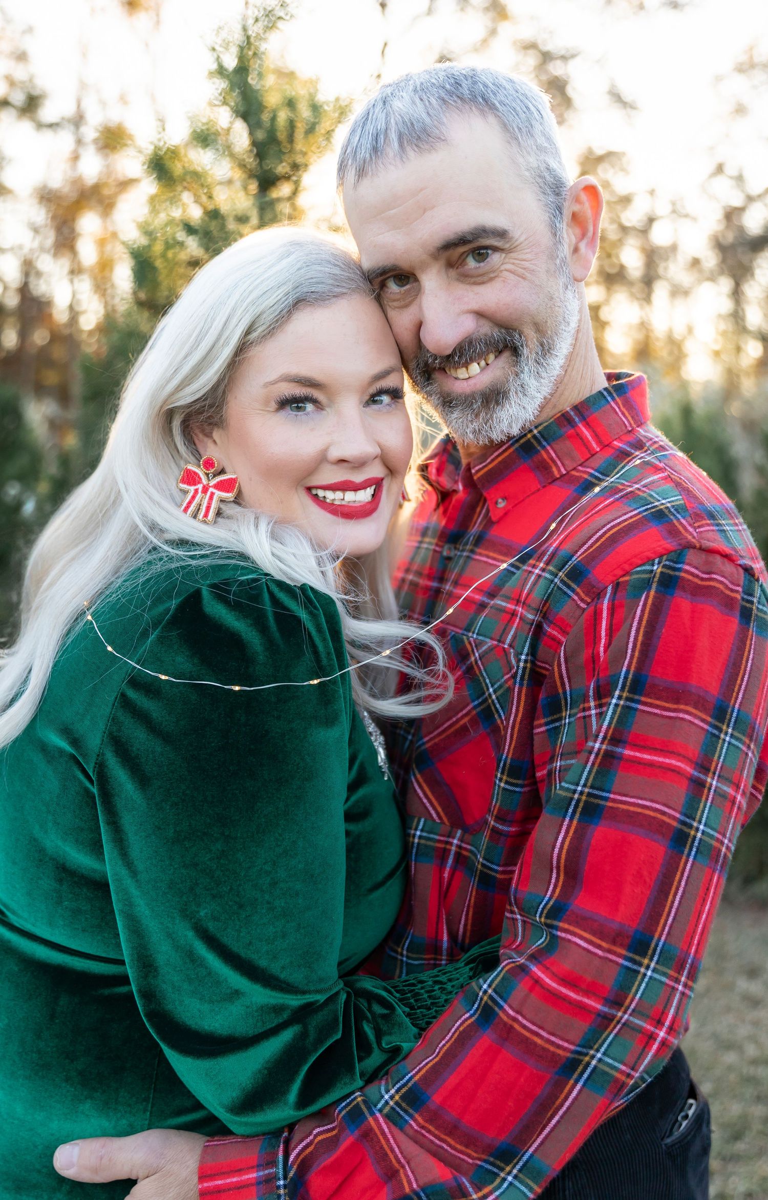 Holiday portrait of couple in coordinating red plaid and green velvet against evergreen background.