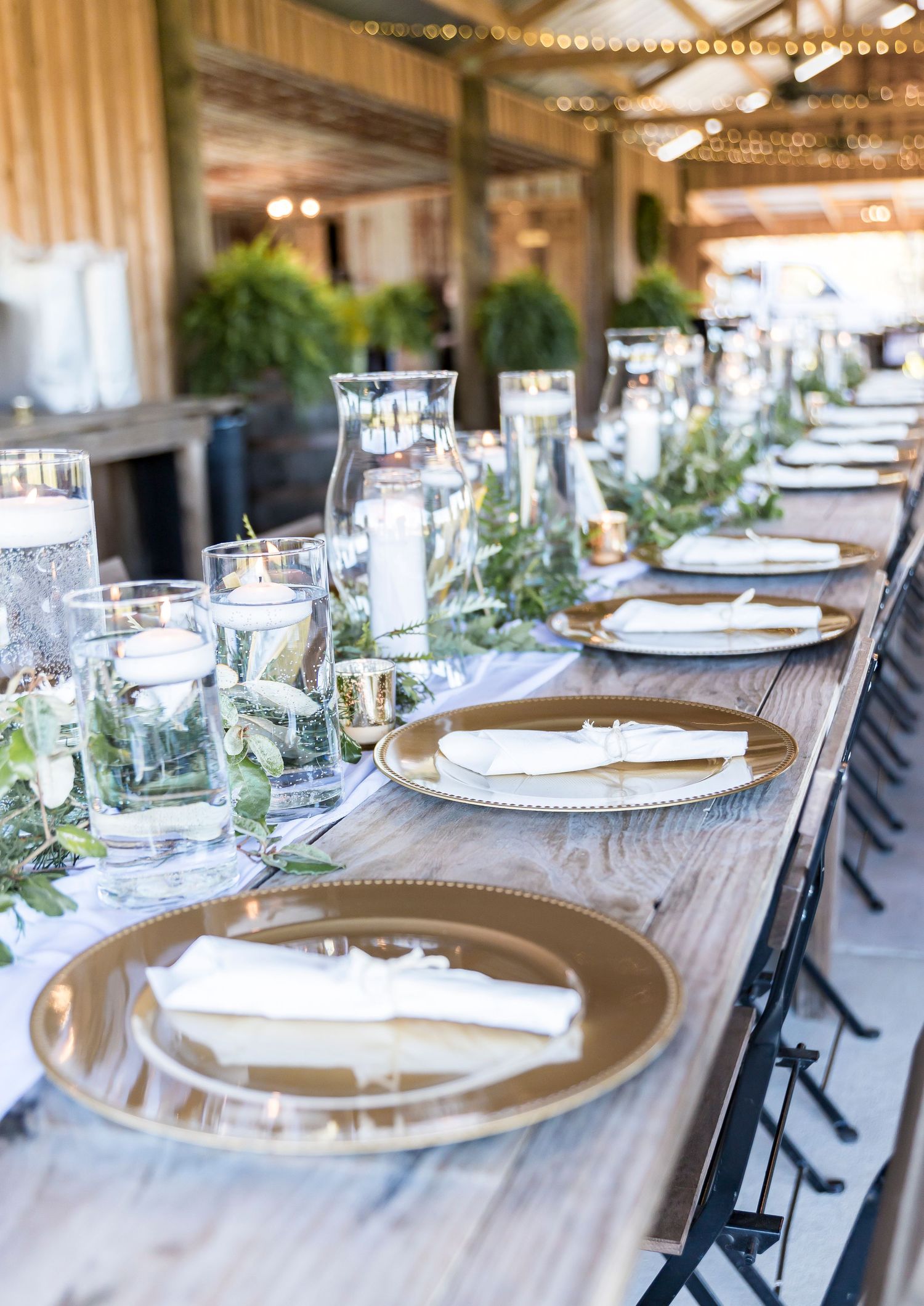 Rustic wedding reception table with gold place settings and glass centerpieces.