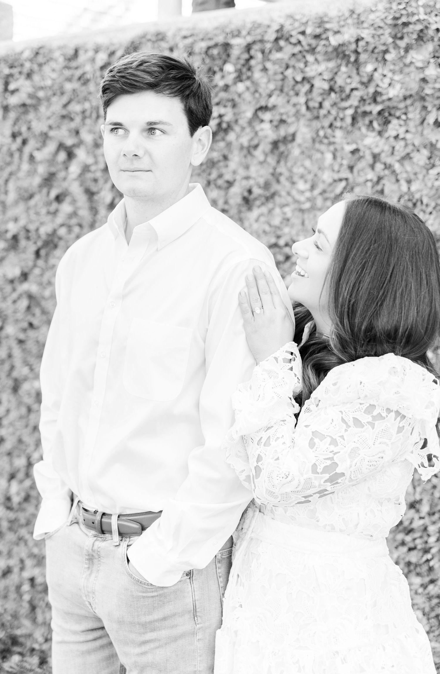 Black and white portrait of couple in white clothing posing against an ivy wall.