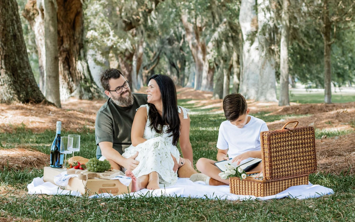 Family enjoying an outdoor picnic under tall trees in a park.