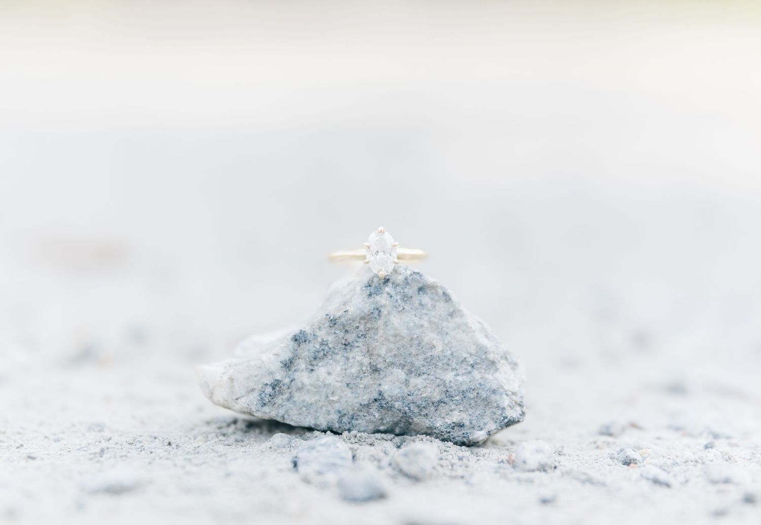 A diamond engagement ring sitting atop a rough grey stone or mineral surface.