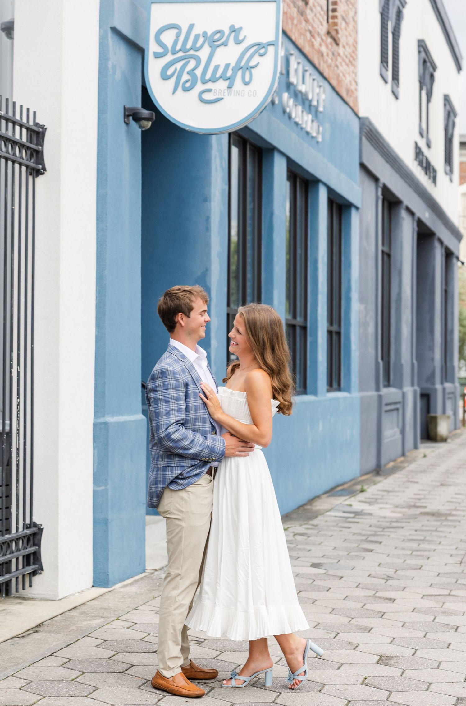 Couple embracing outside Silver Bluff brewery's blue exterior wall on a cobblestone sidewalk.