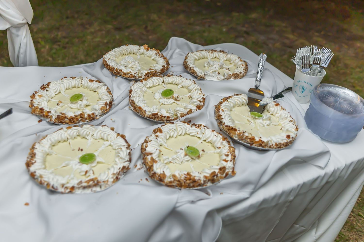 Display of artisanal tarts or pies arranged on white tablecloth for wedding dessert table.