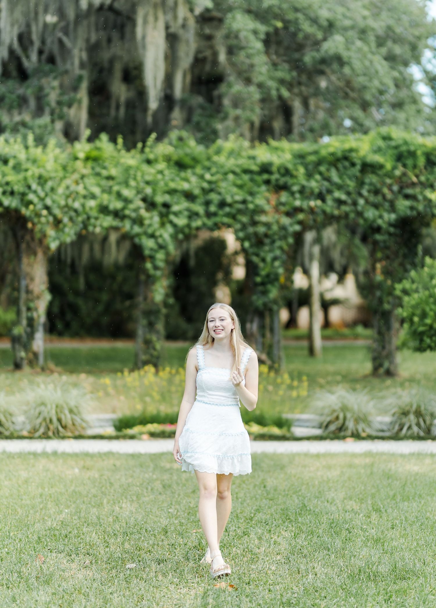 A scenic portrait in a white dress against Spanish moss and greenery in a Southern garden setting.