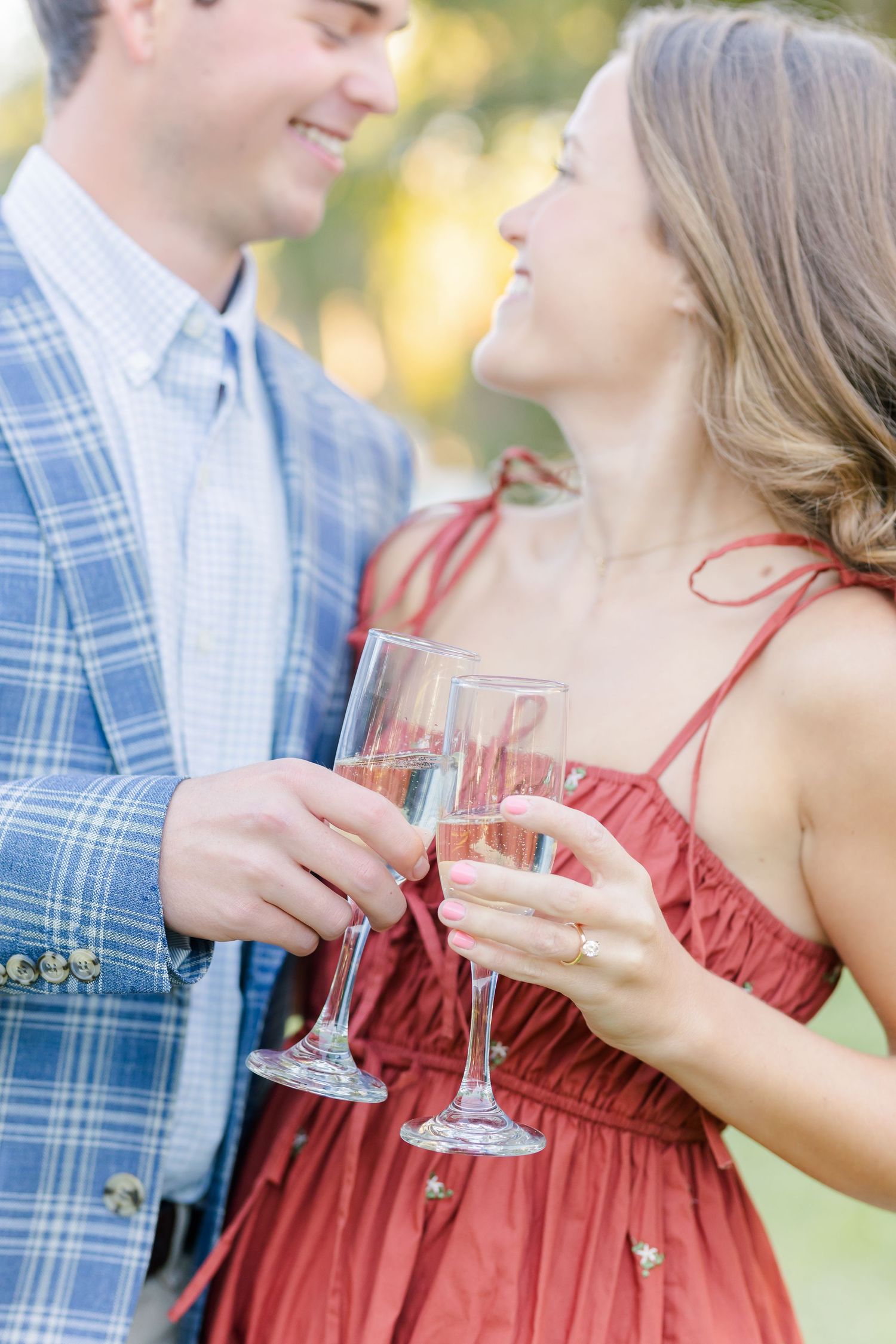 A couple in blue and red attire shares a romantic moment while holding wine glasses outdoors.