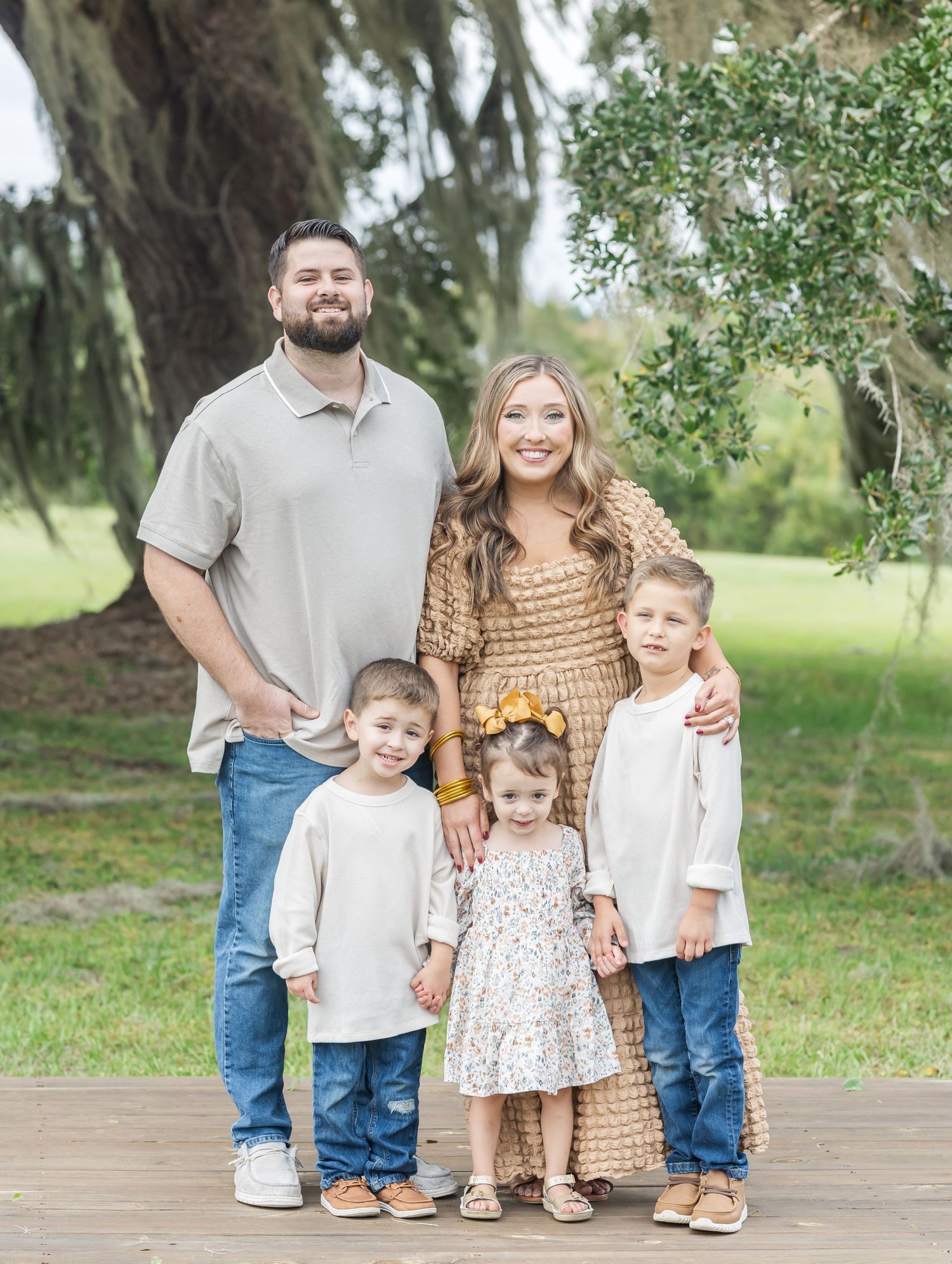 Family portrait session on wooden deck with natural greenery backdrop.